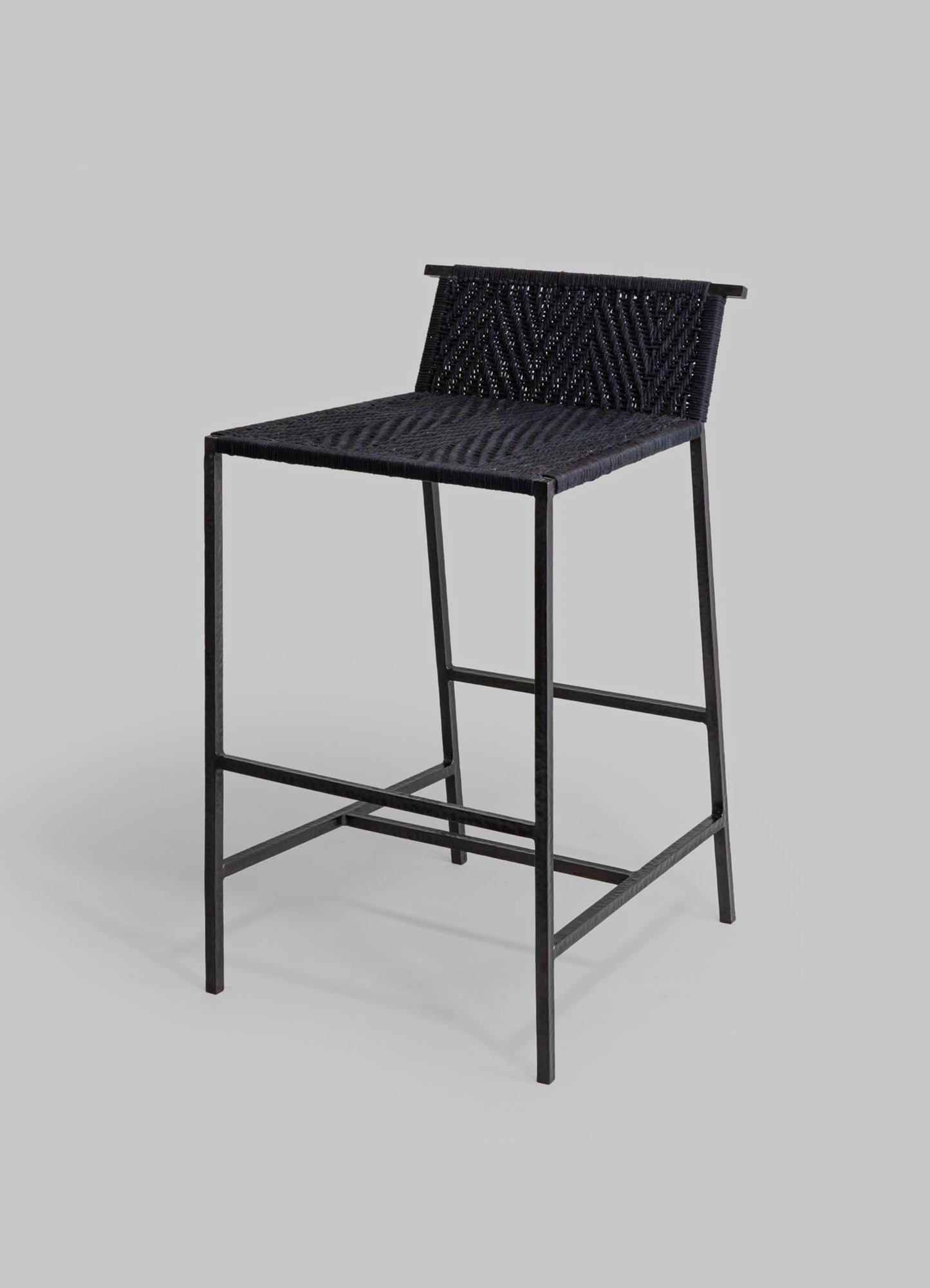 A black woven bar stool with a metal frame, featuring a textured seat and backrest with intricate geometric weaving, set against a plain gray background.