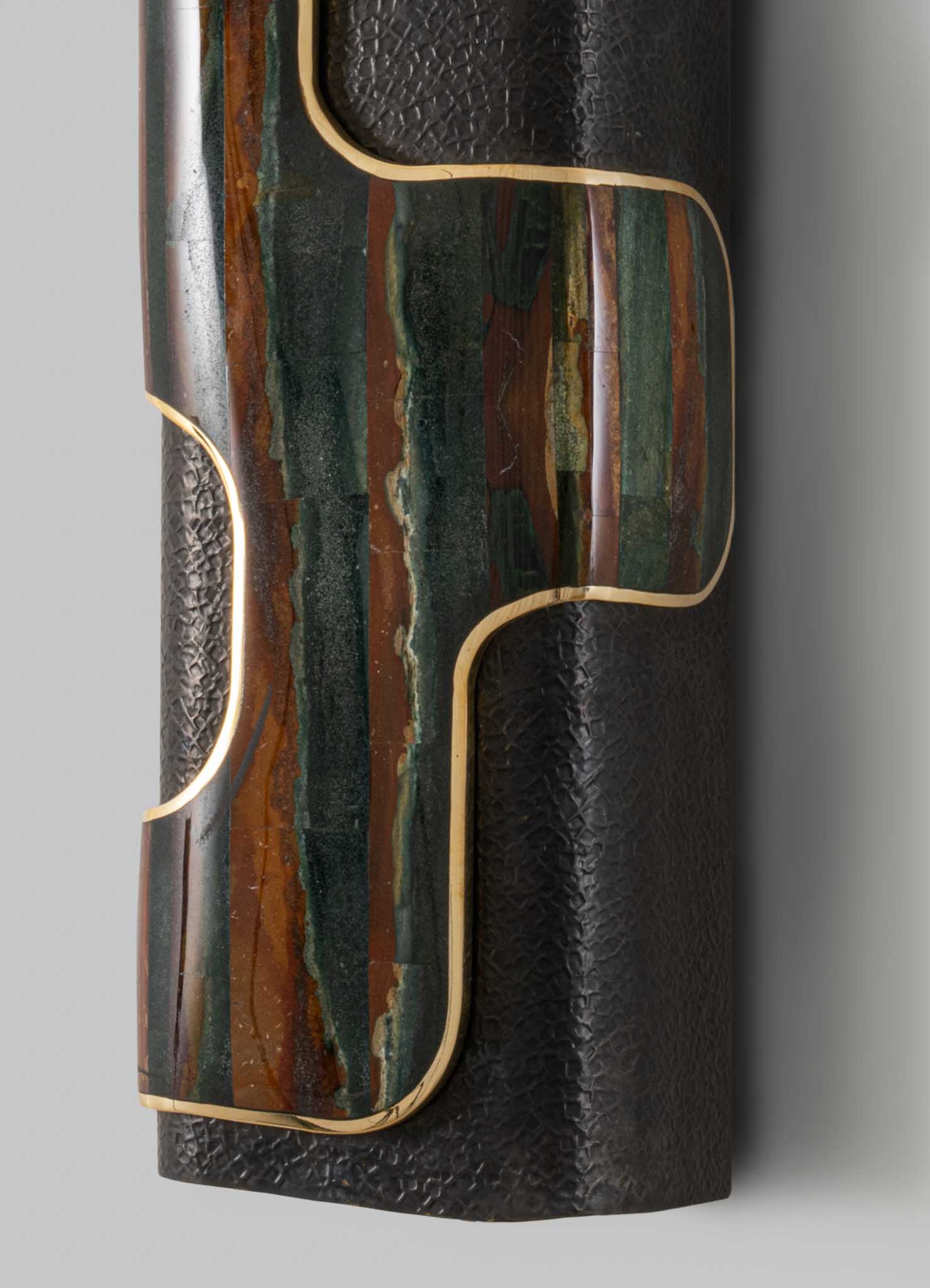 A decorative table visible in the image, featuring a top surface with a multicolored, abstract pattern in shades of green, brown, and cream, framed by a thin gold trim. The main body appears to be made of black textured material, possibly leather or faux leather, with a subtle pattern.