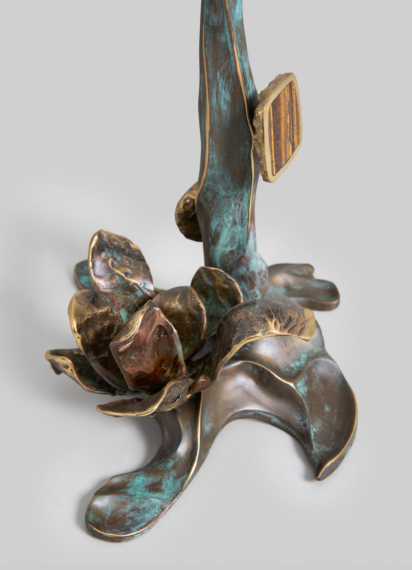A decorative metal sculpture featuring organic, floral-inspired forms with a combination of bronze, turquoise patina, and gold-toned accents, evoking a handcrafted, artistic style. The piece has flowing, natural lines and textured surfaces, creating a rustic and artistic visual mood.
