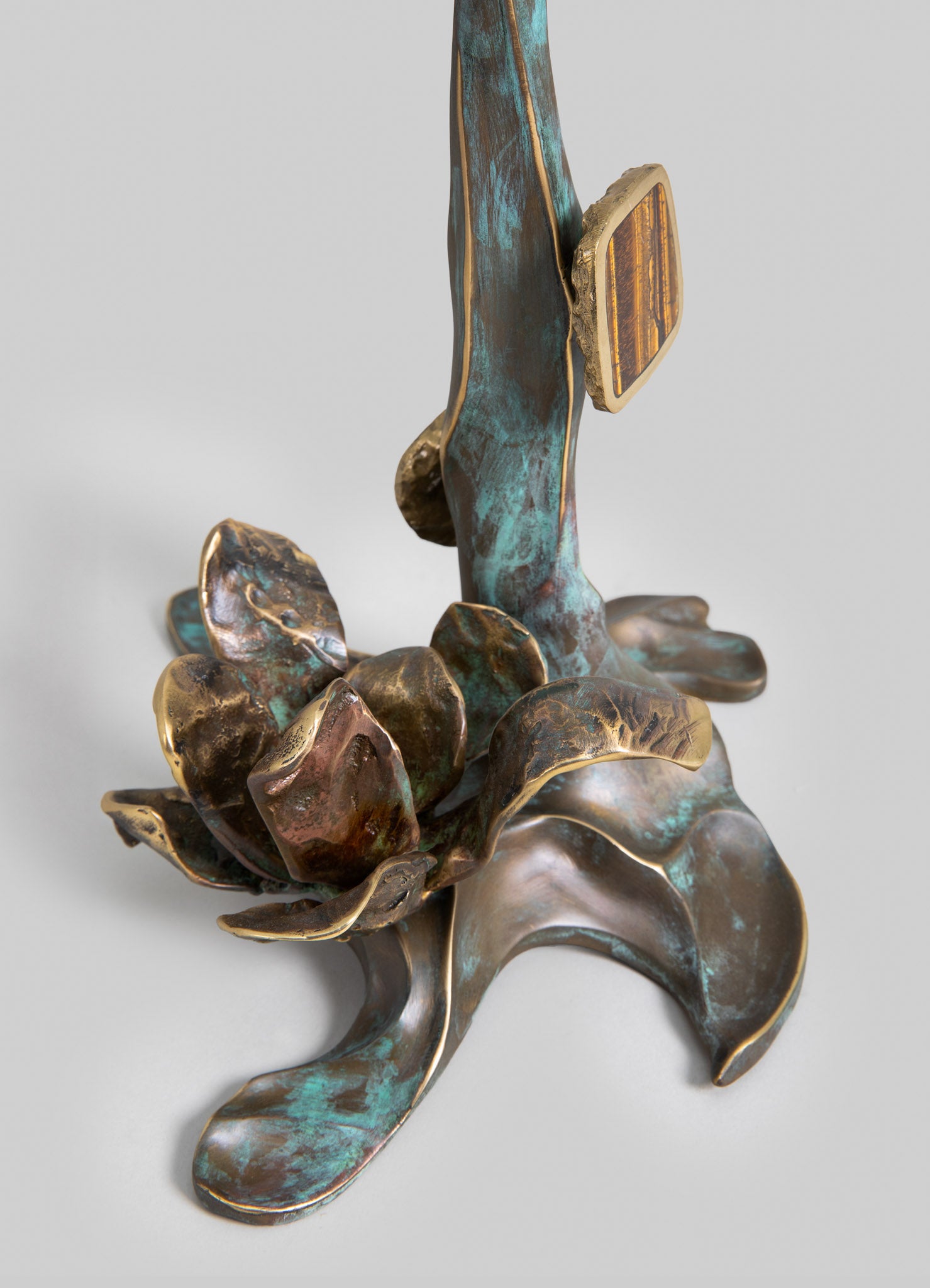 A decorative metal sculpture featuring organic, floral-inspired forms with a combination of bronze, turquoise patina, and gold-toned accents, evoking a handcrafted, artistic style. The piece has flowing, natural lines and textured surfaces, creating a rustic and artistic visual mood.