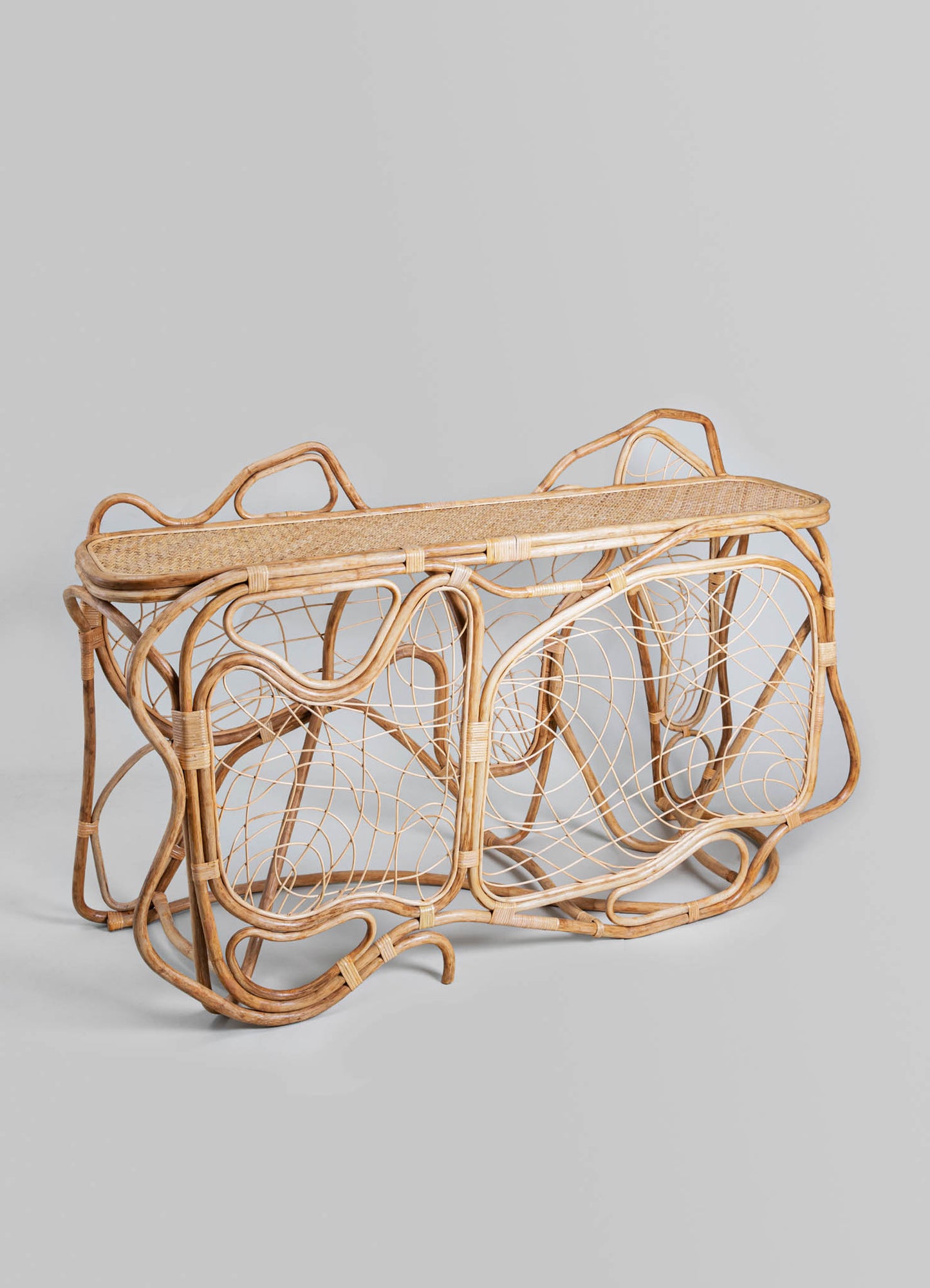 A woven wicker magazine rack with an intricate, curvilinear design and natural wood tones, featuring a rectangular top surface and open sides with circular motifs.