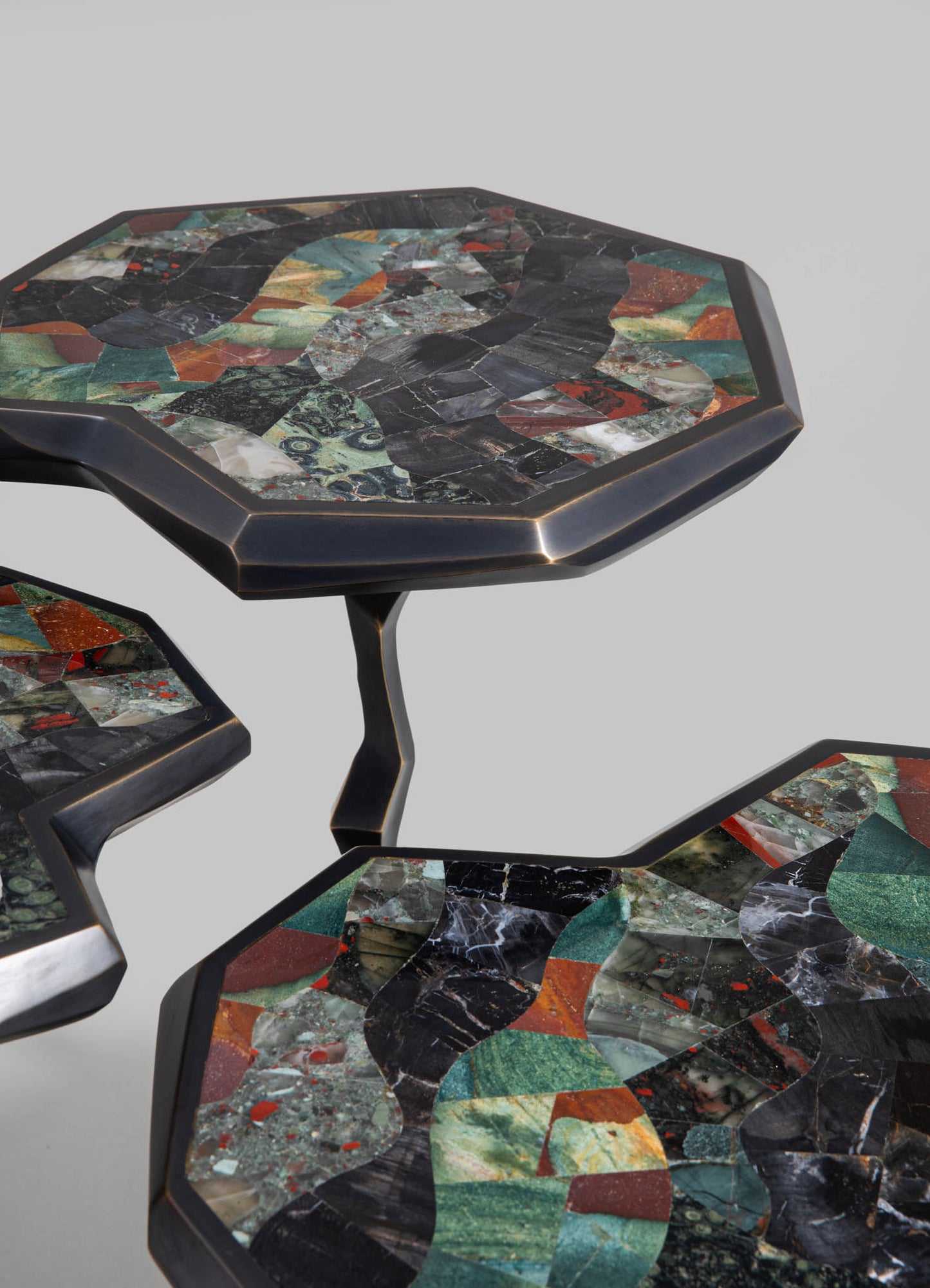 Set of three nesting side tables with mosaic marble tops featuring abstract geometric patterns in shades of black, green, red, and cream, with dark metal frames and sculptural, angular legs.