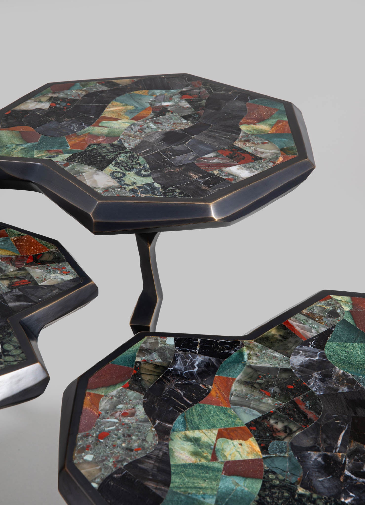 Set of three nesting side tables with mosaic marble tops featuring abstract geometric patterns in shades of black, green, red, and cream, with dark metal frames and sculptural, angular legs.