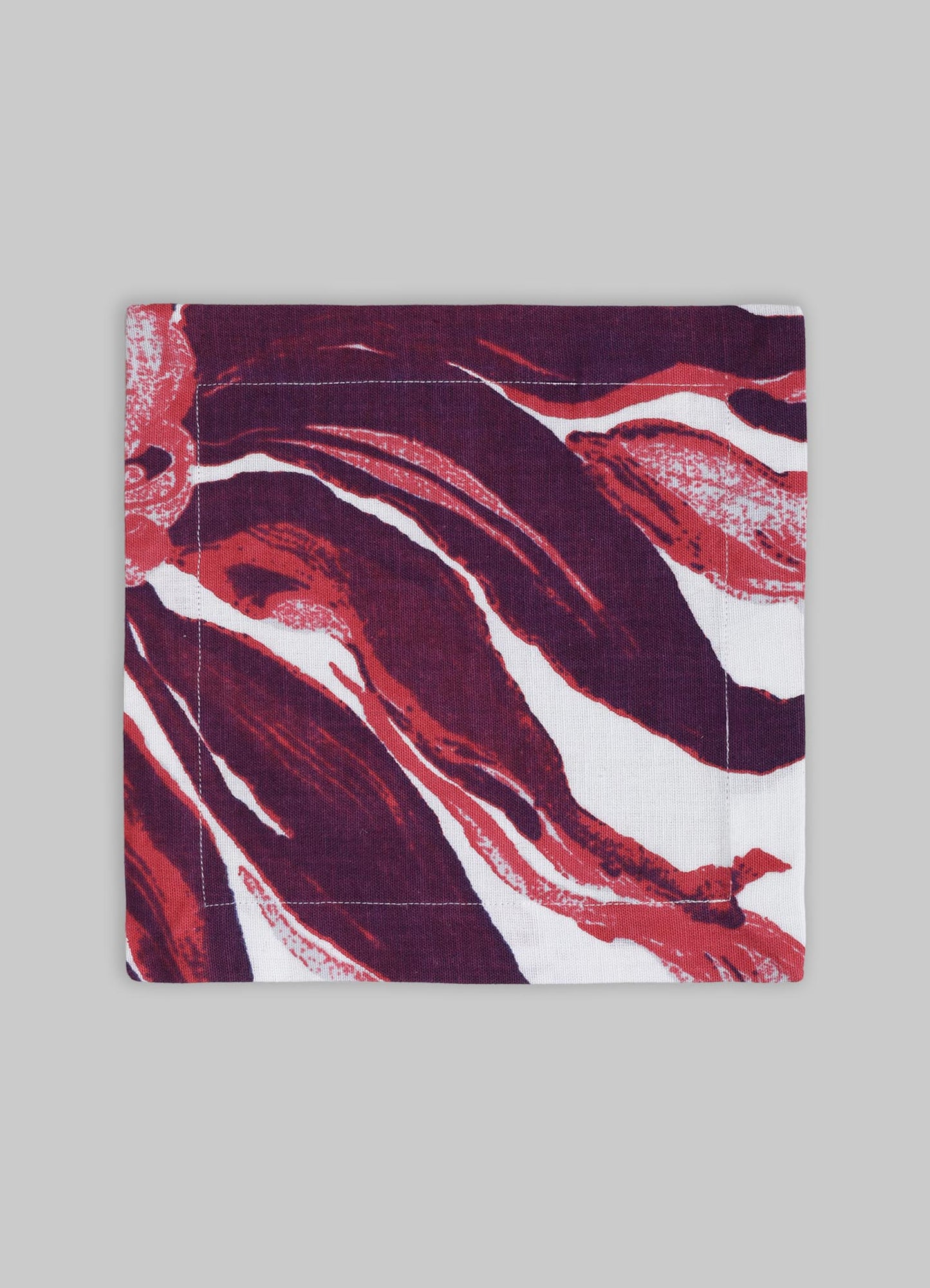 Printed fabric napkin with an abstract floral motif in shades of deep red, burgundy, and white, made from cotton or linen material, displayed on a plain gray background.