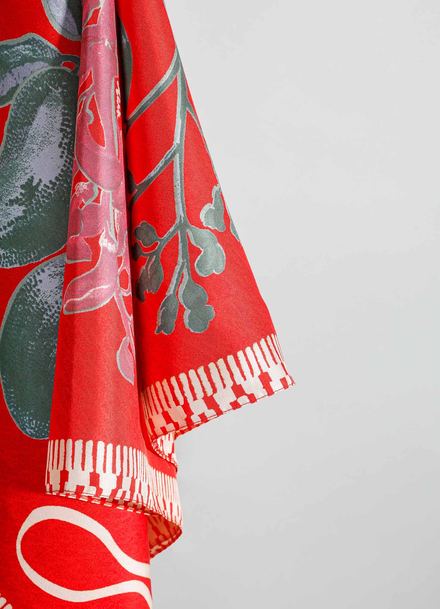 Fabric with a vibrant red background featuring a floral motif in shades of pink and green, bordered by a geometric white and red pattern, likely a textile or garment. The fabric appears lightweight and has a contemporary style.