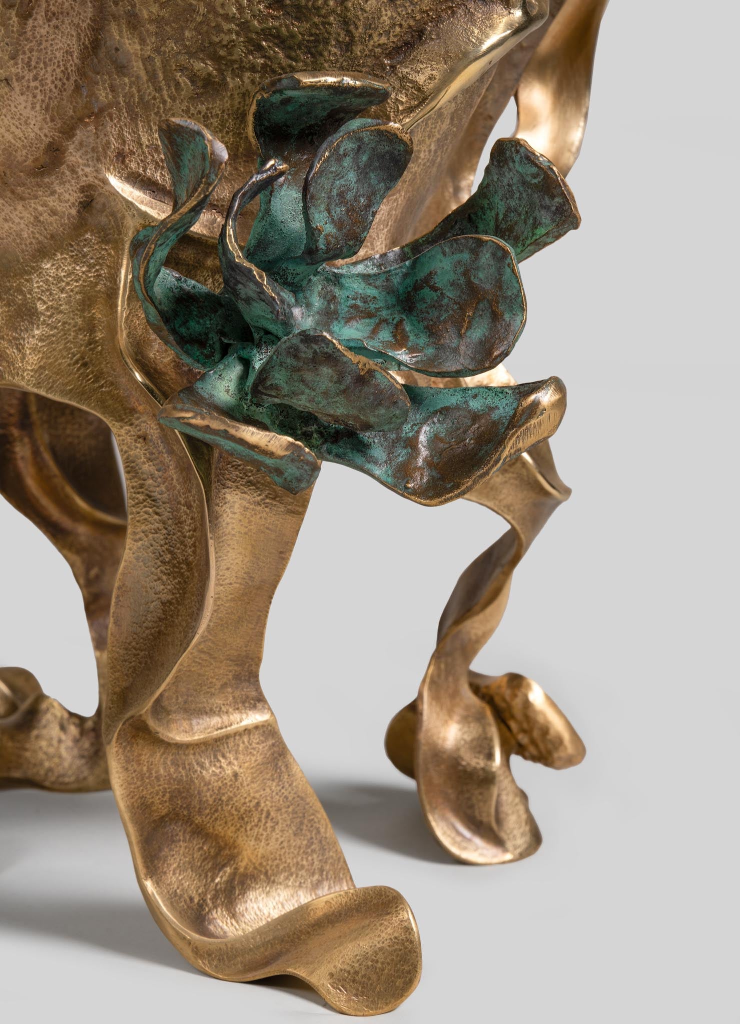 Decorative sculpture featuring a textured brass base with an organic, flowing form, adorned with a bronze patina and a greenish-blue patinated metal leaf motif. The overall style is artisanal and sculptural, with an emphasis on handcrafted, natural-inspired design.