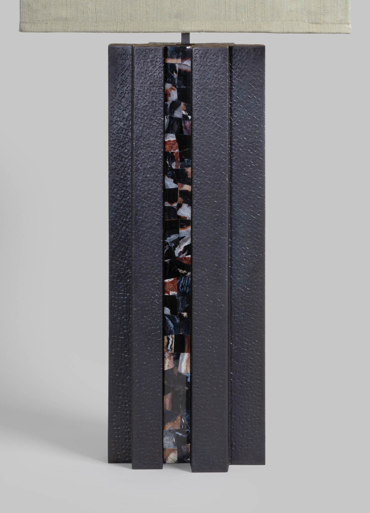 A table lamp with a textured black ceramic body featuring a vertical strip of multicolored marble pattern, topped with a rectangular fabric lampshade in a light neutral tone.