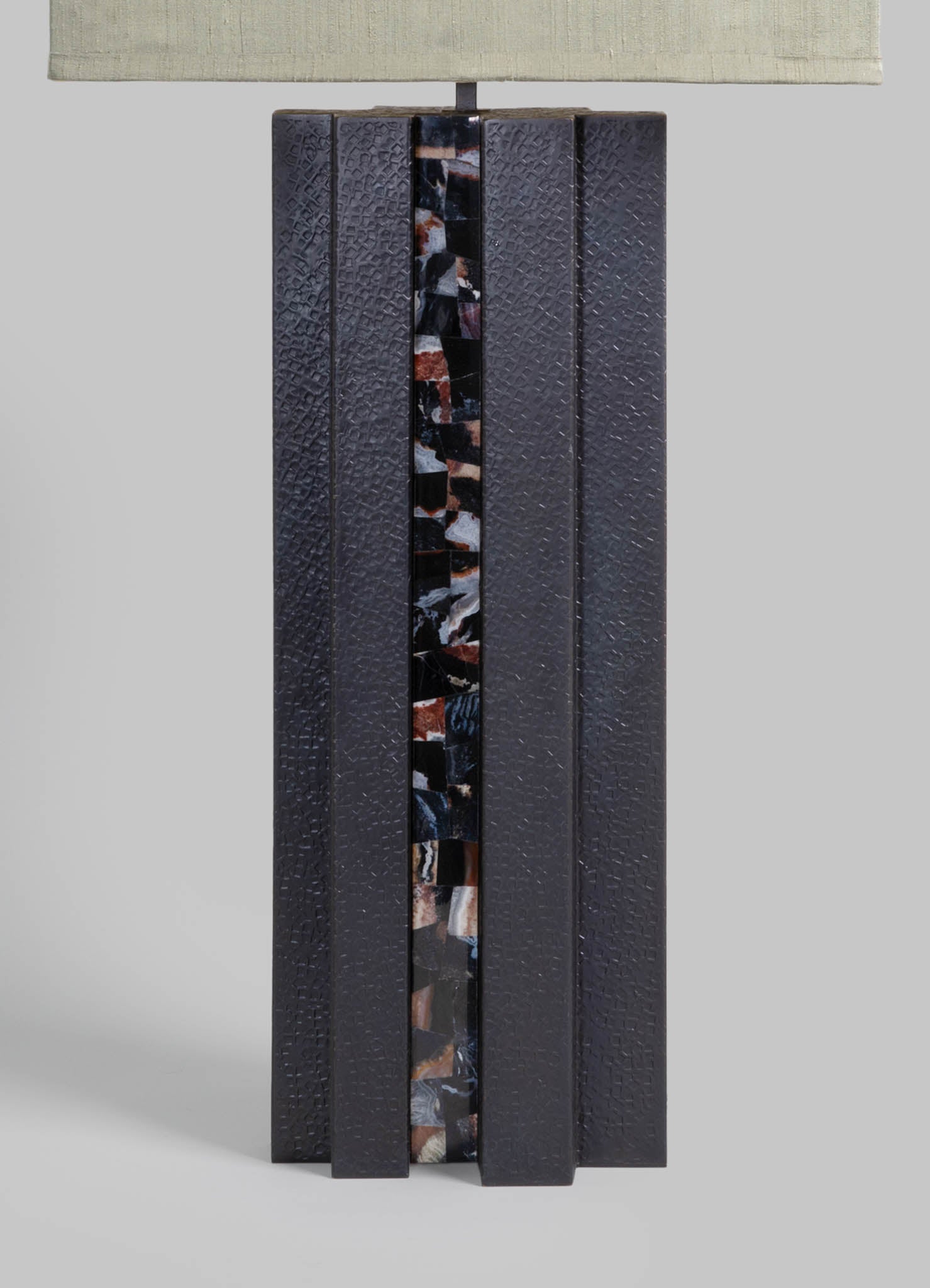 A table lamp with a textured black ceramic body featuring a vertical strip of multicolored marble pattern, topped with a rectangular fabric lampshade in a light neutral tone.