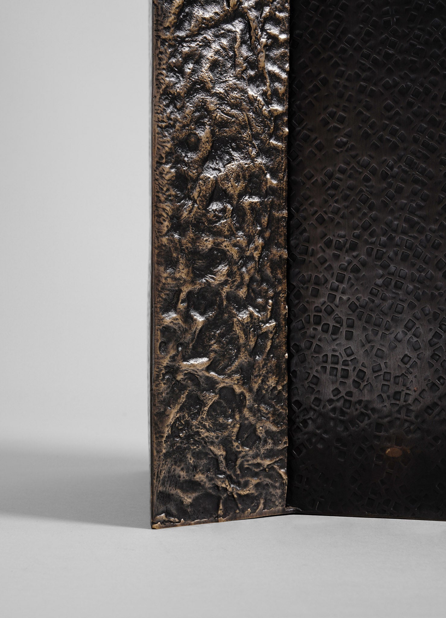 Metallic textured wall panel with a rough, hammered surface in dark bronze and black tones, featuring an abstract, organic pattern. The style is contemporary with a rustic, industrial finish.