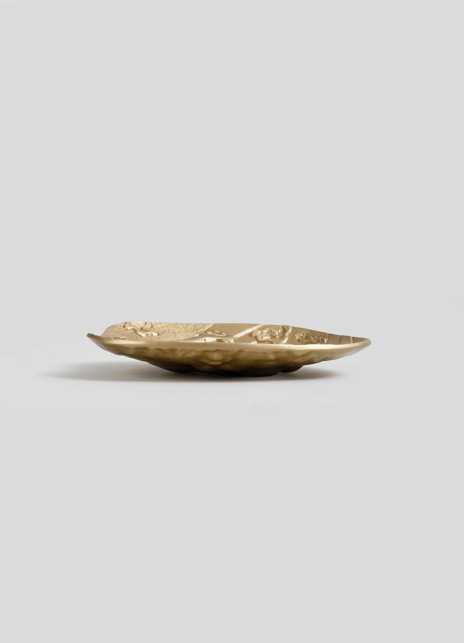 A shallow bowl made of metallic material with a textured, uneven surface and an antique gold finish.