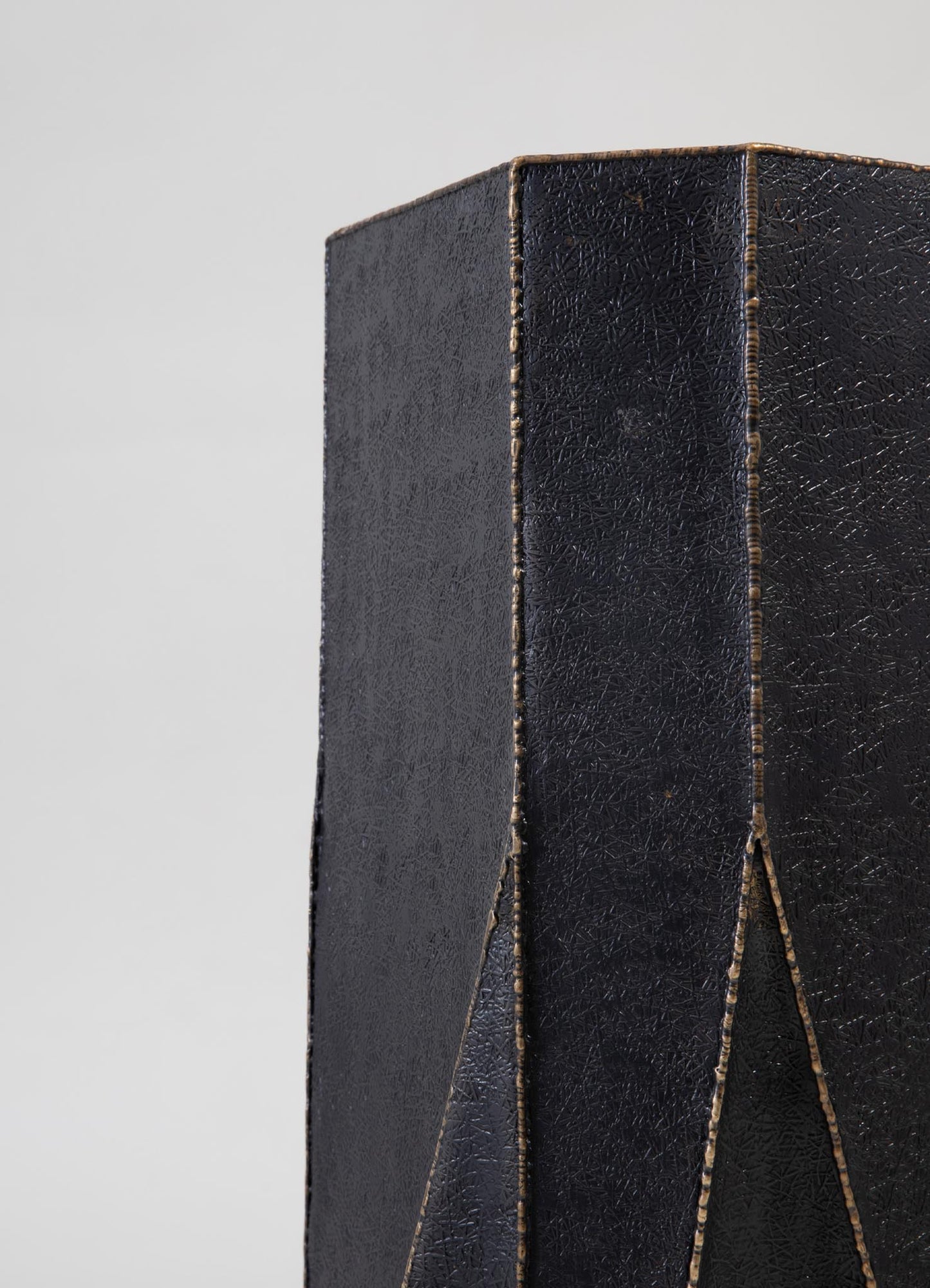 A black leather-bound item with a textured surface and decorative stitched edges, featuring a geometric pattern created by intersecting lines.