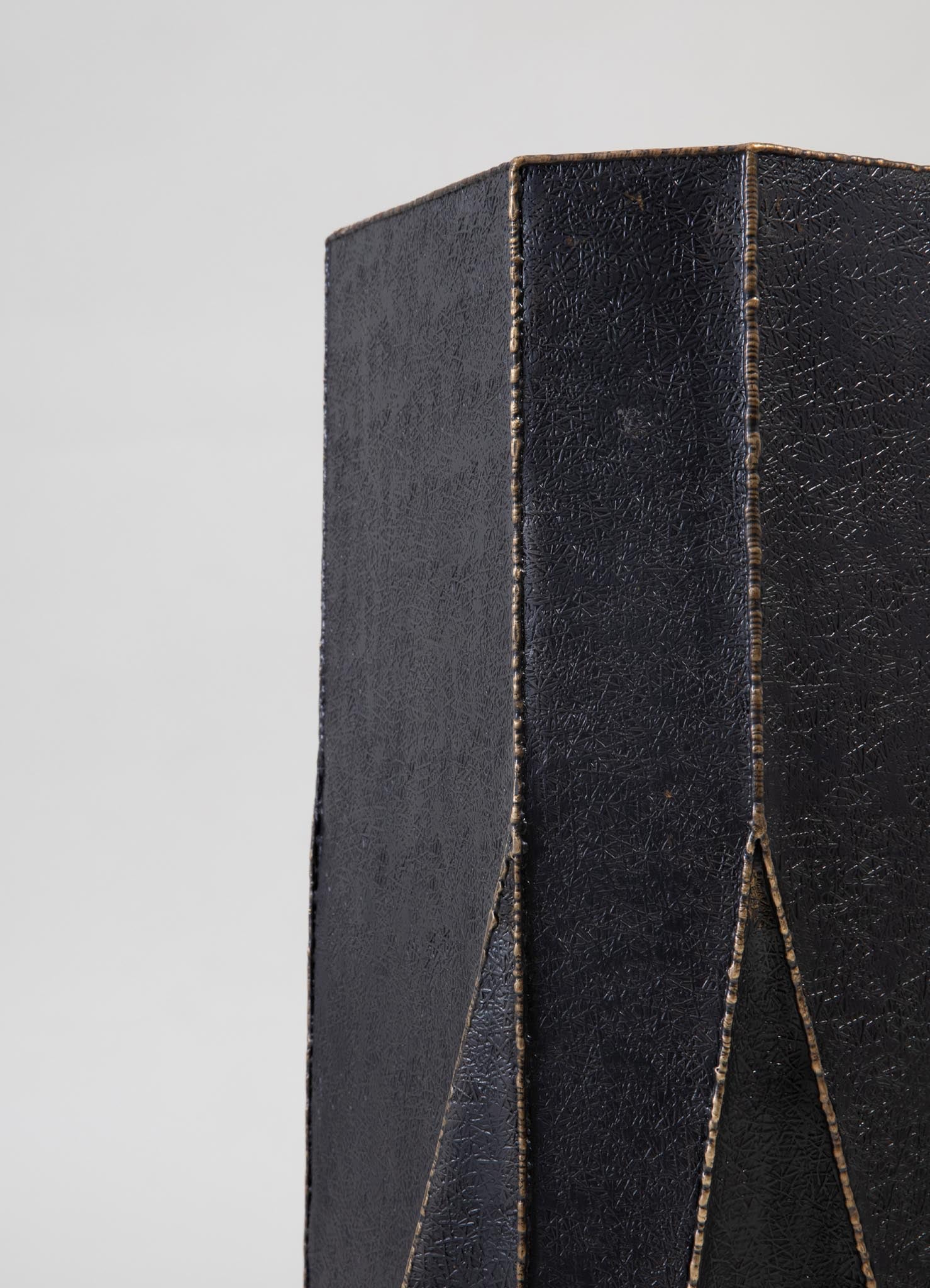 A black leather-bound item with a textured surface and decorative stitched edges, featuring a geometric pattern created by intersecting lines.