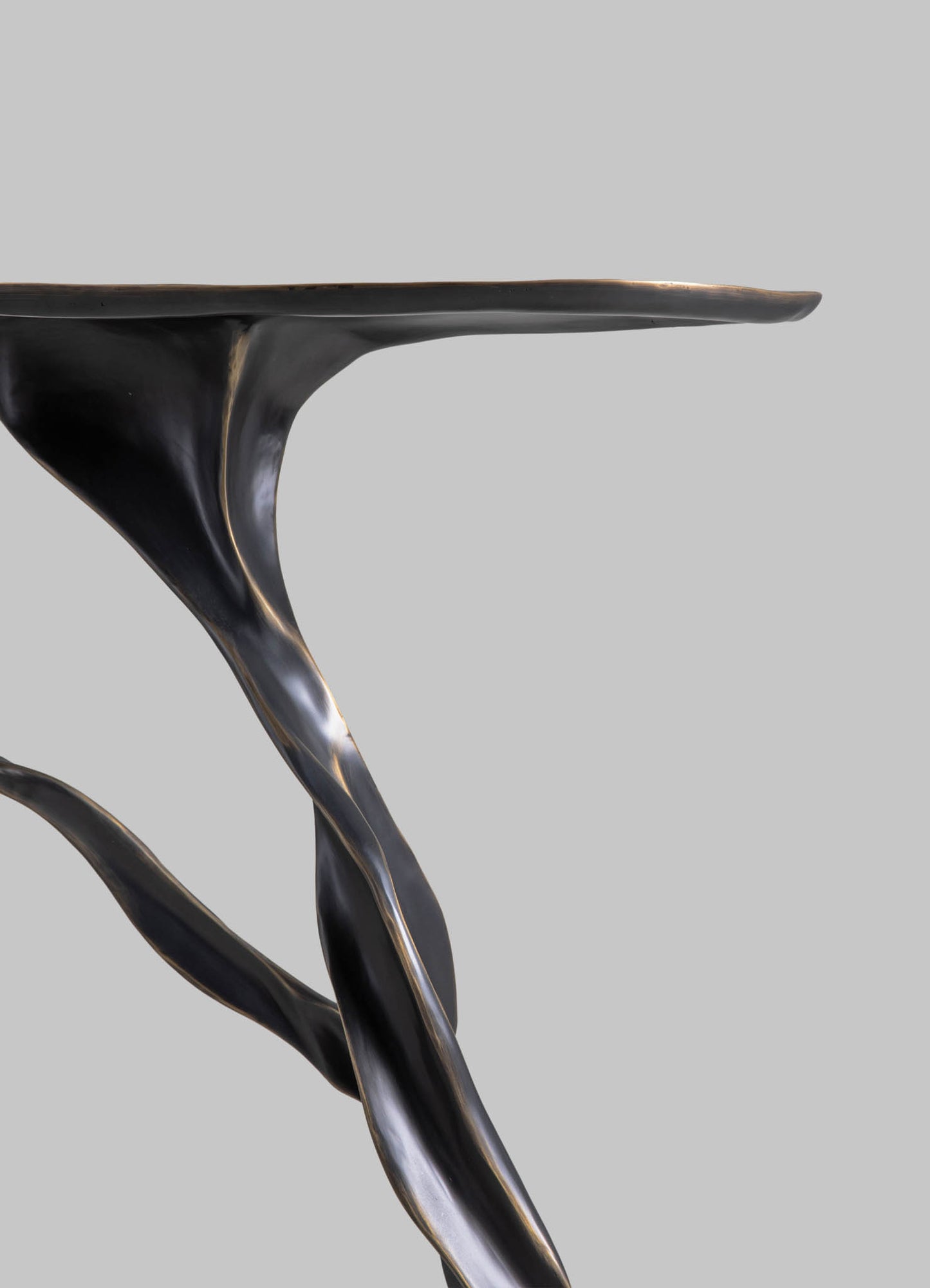 A close-up of a black, polished metal side table featuring sculptural, twisting legs with a smooth, reflective surface and a matte gray background.