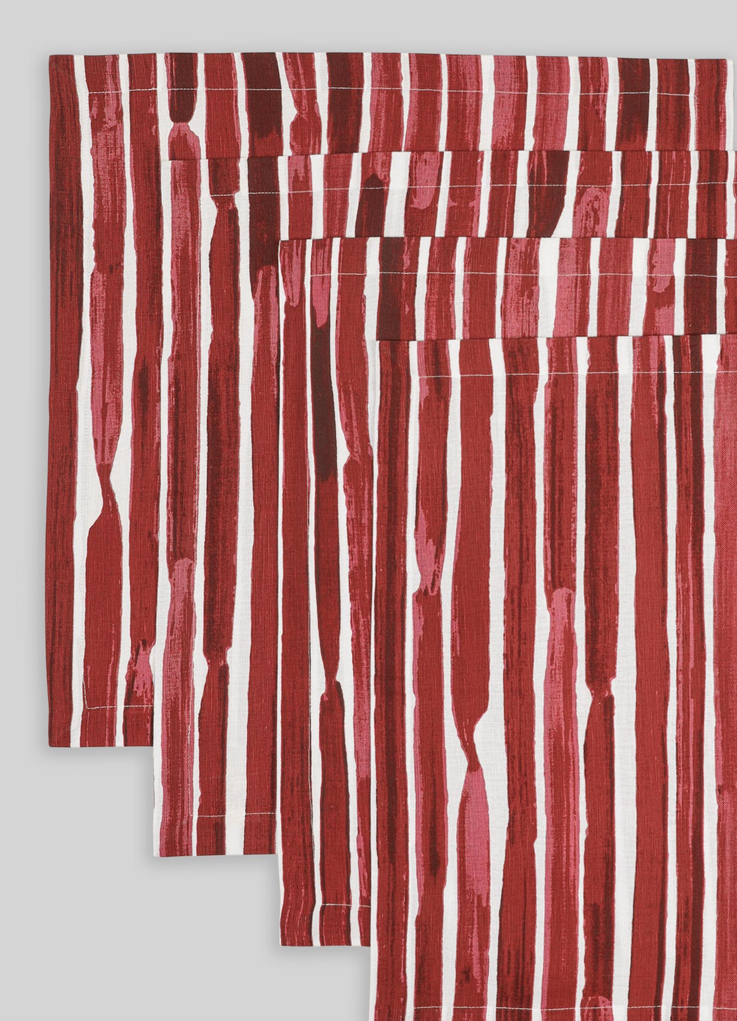 Red and white striped table linens with abstract, hand-painted motifs on a cotton fabric, featuring a contemporary and vibrant design. The pattern consists of irregular vertical and horizontal brushstrokes creating a bold, artistic look.