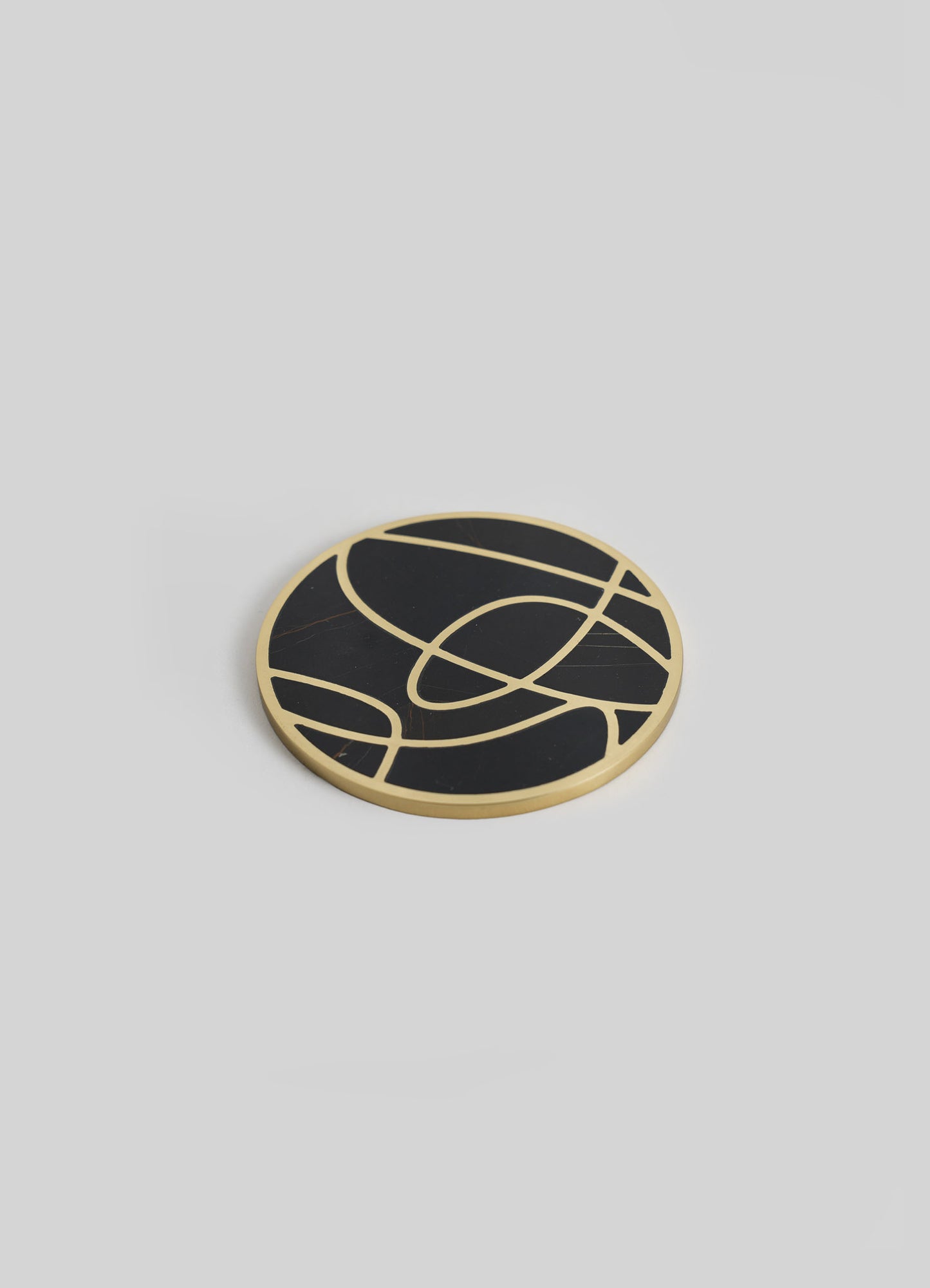 A round coasters with a black marble surface and gold geometric pattern, featuring curved lines and abstract motifs.