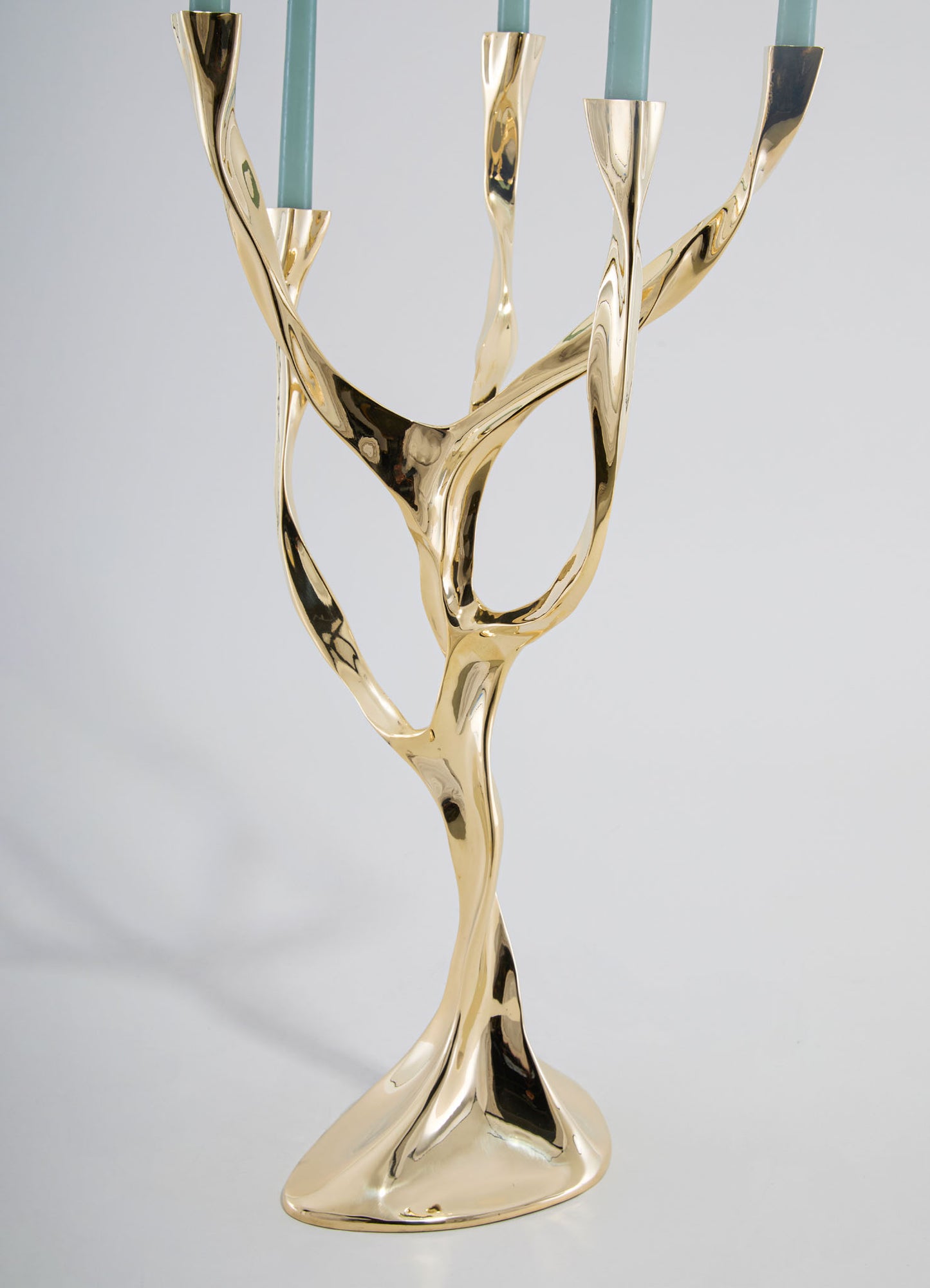 A brass candlestick holder with an organic, sculptural design featuring flowing, twisted lines and a polished gold finish, holding light blue candles.