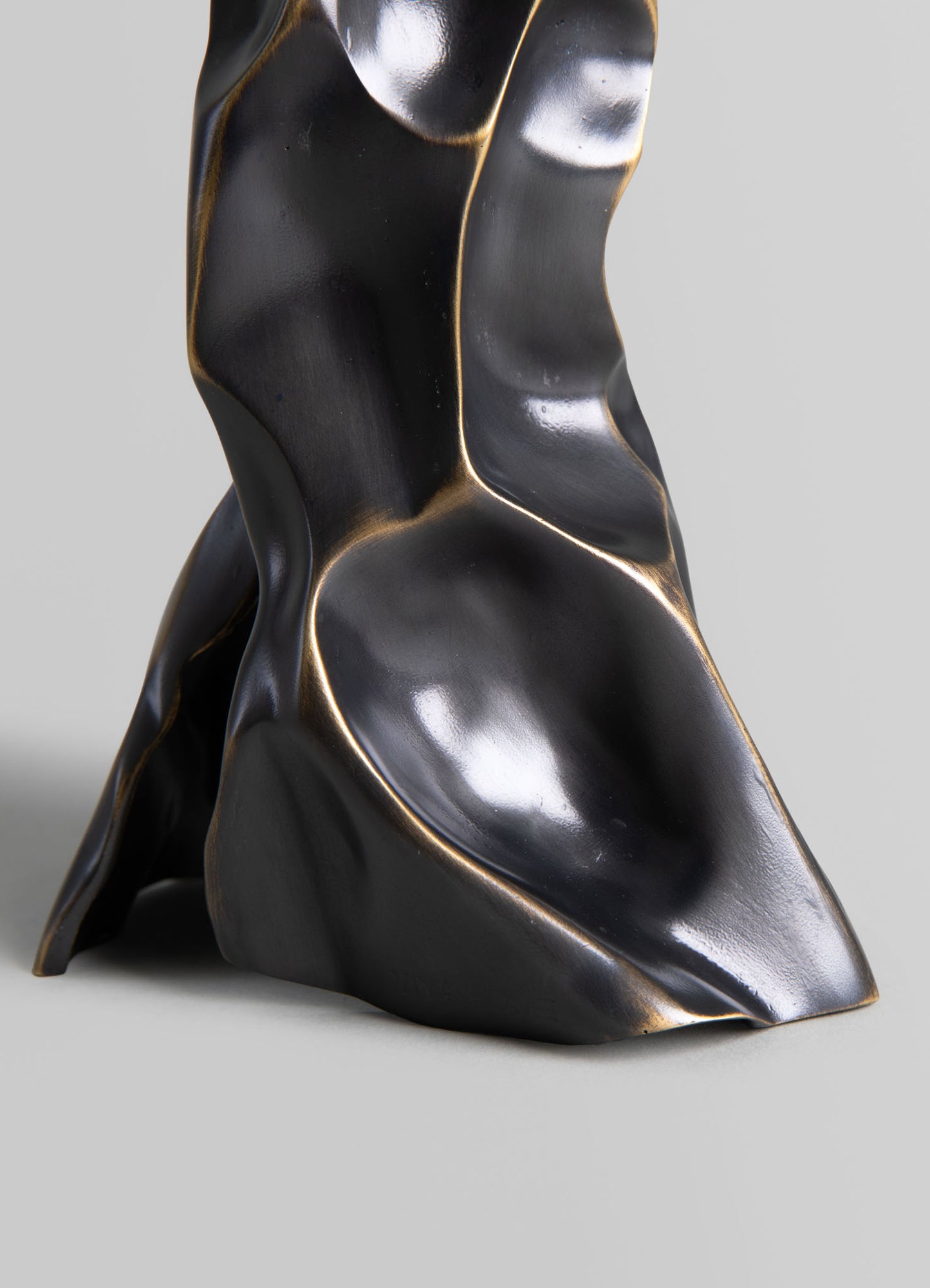 A sculptural decorative object made of black and gold-toned metal with organic, flowing curves and an abstract, modern form.