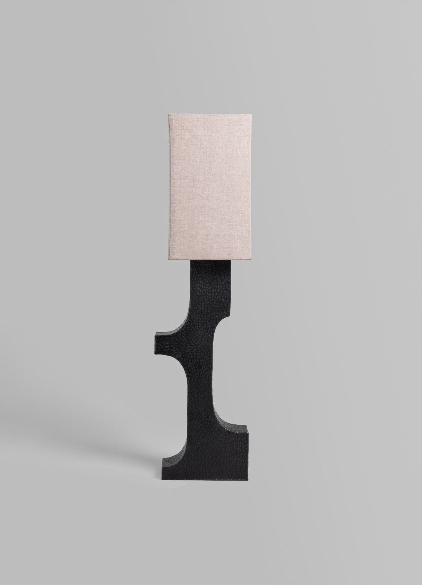 A modern table lamp with a rectangular fabric shade in soft beige and a sculptural black base with a textured surface.
