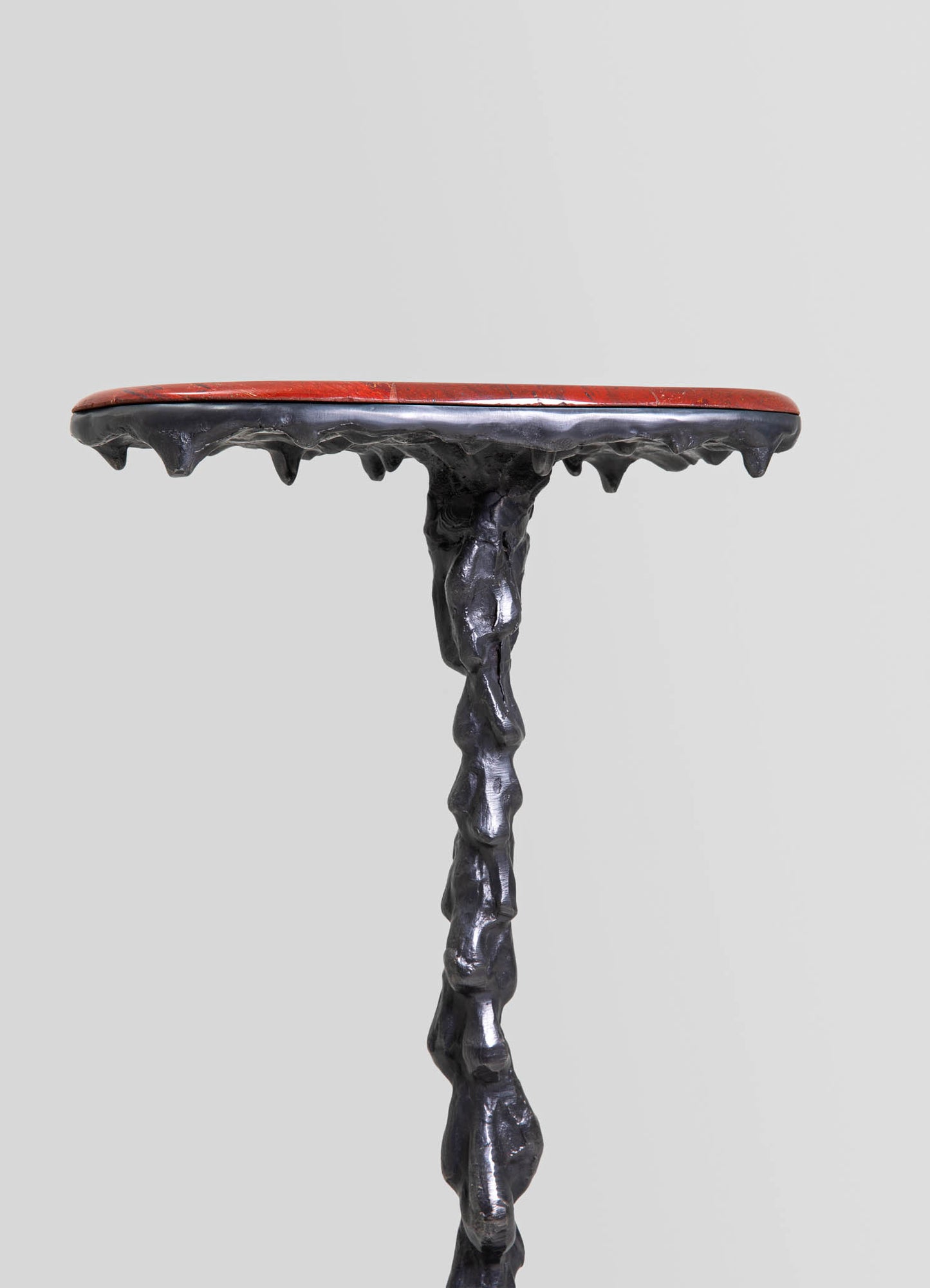 A side table with a textured, black irregularly shaped wooden base and a round red marble top, combining rustic and contemporary design styles.