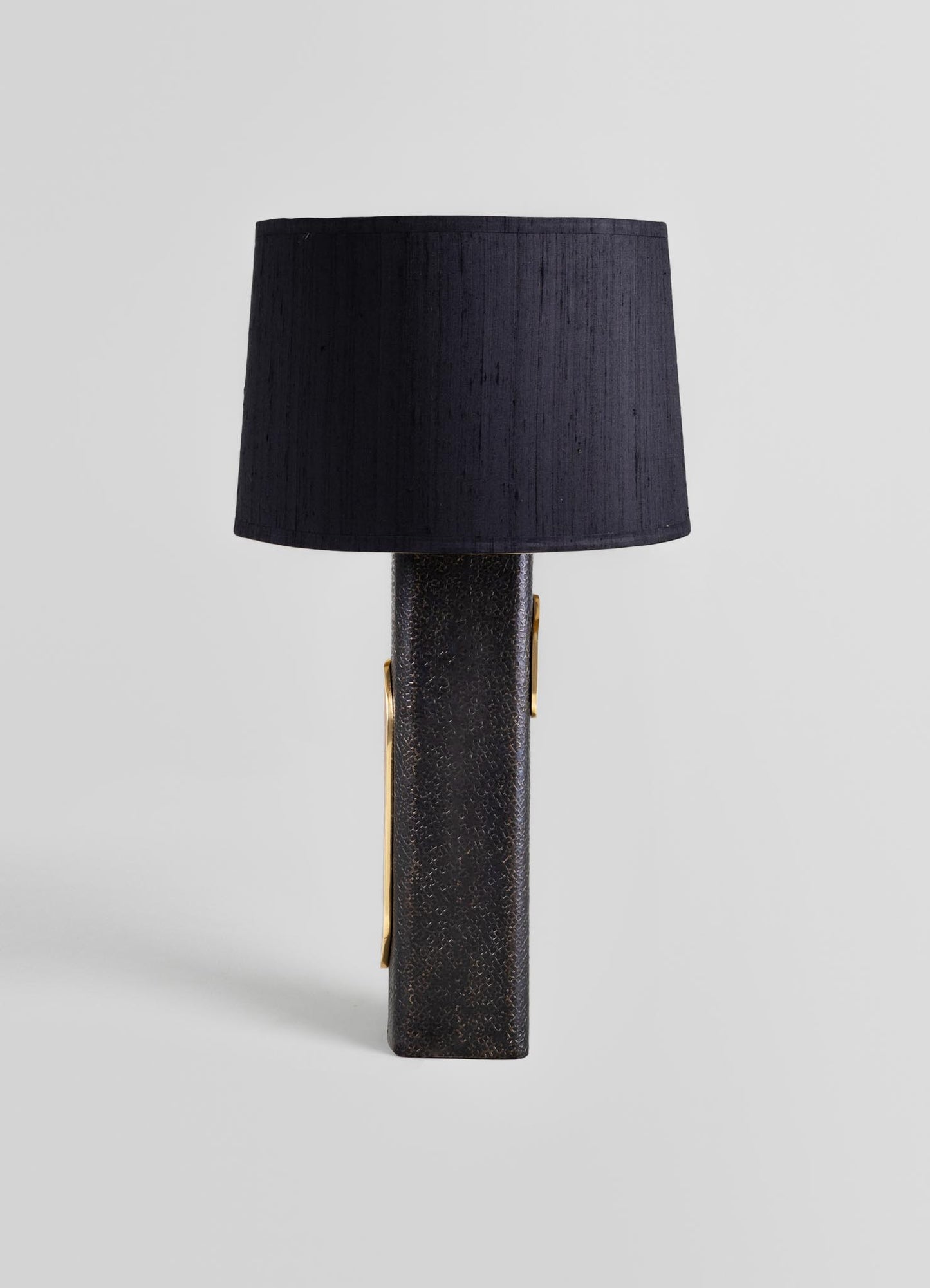 A table lamp with a textured black base featuring gold accents and a cylindrical black fabric lampshade, displayed against a plain light background.