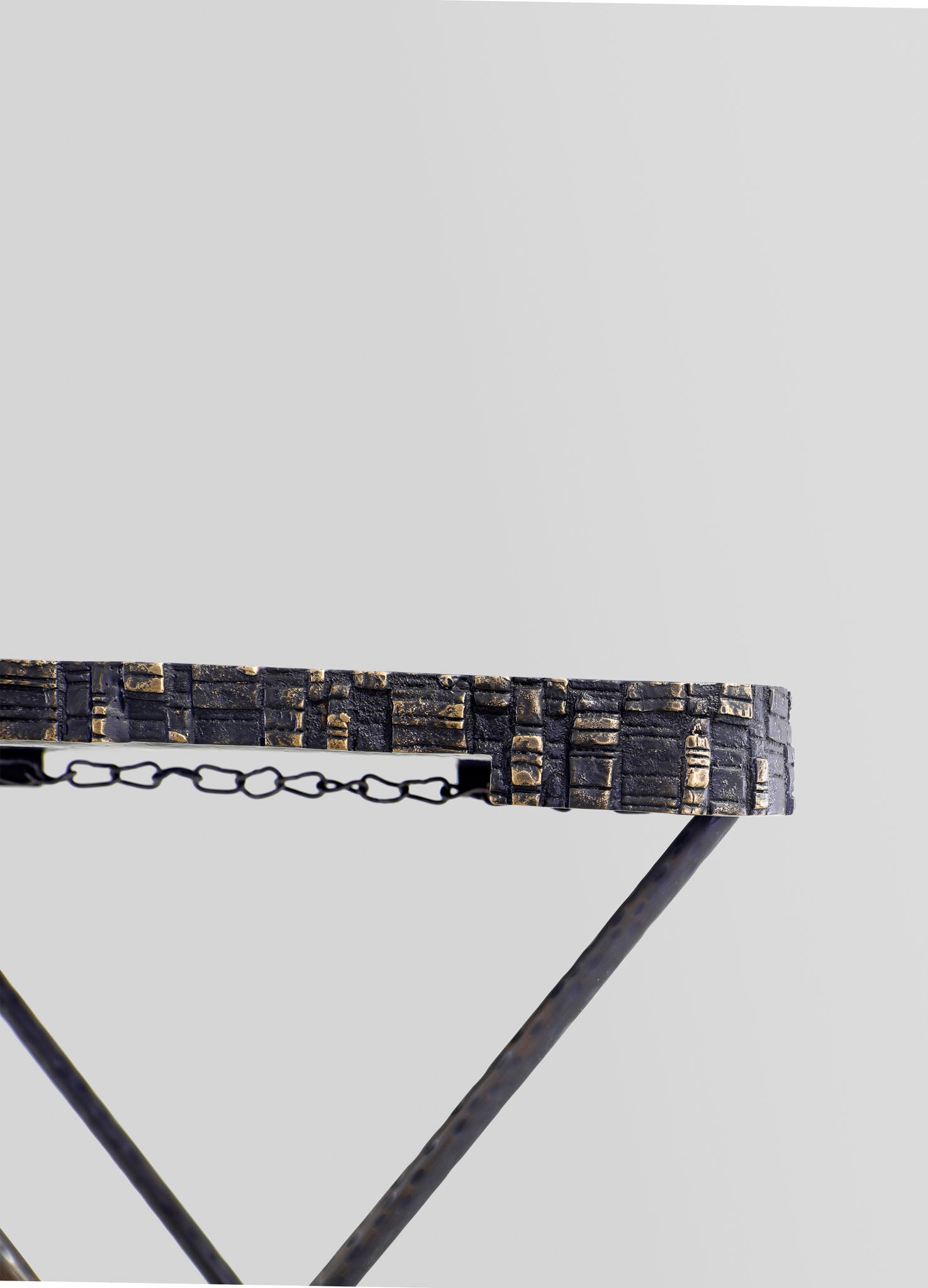 A close-up of a table with a textured, dark-colored brick or stone surface and an antique-style chain detail on the edge, supported by slim, dark metal legs.