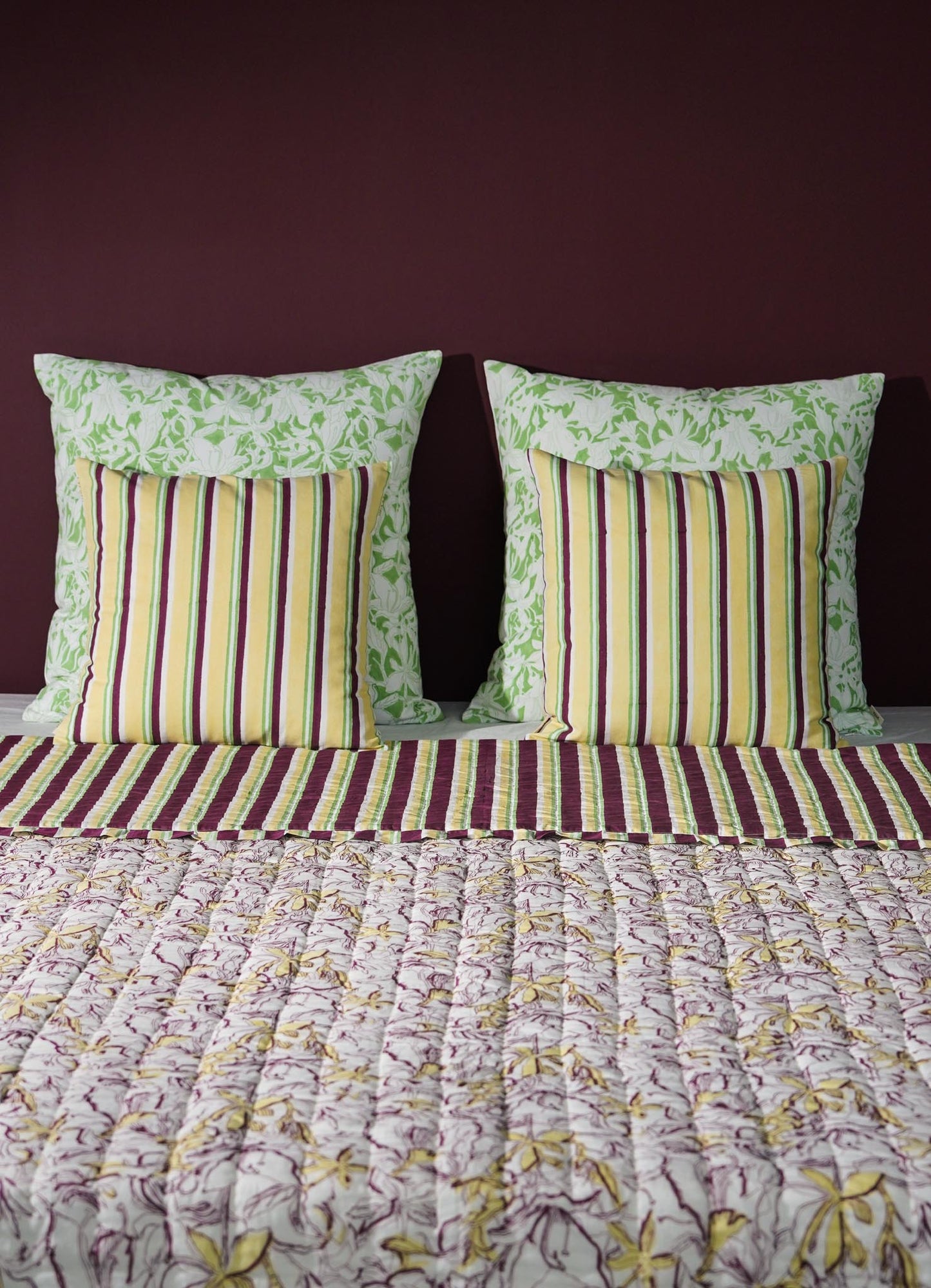 Striped pillows and floral-patterned bedspread on a bed with a dark purple wall luxury cushion cover viya