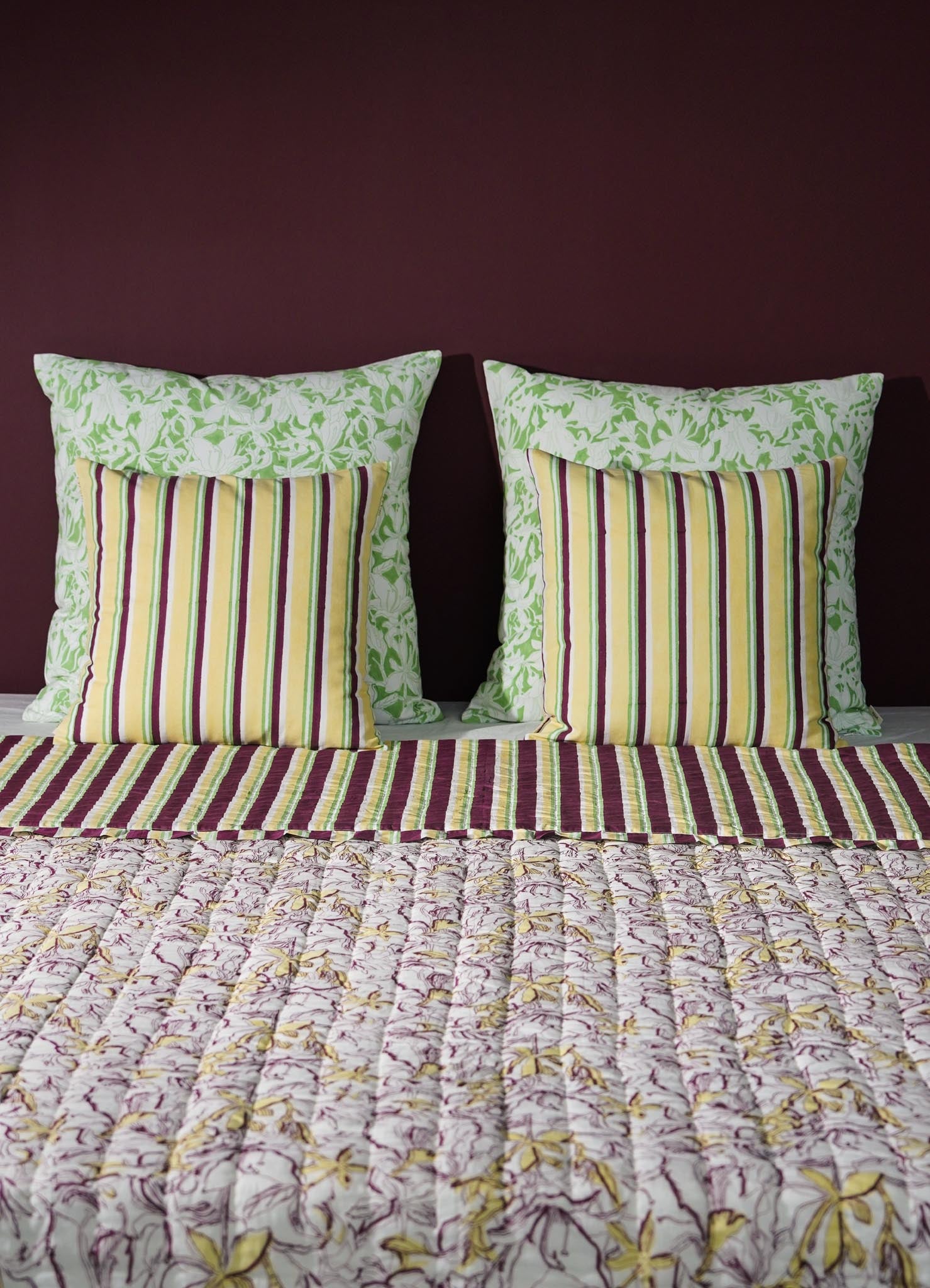 Striped pillows  and floral-patterned bedspread on a bed with a dark purple wall luxury cushion cover viya