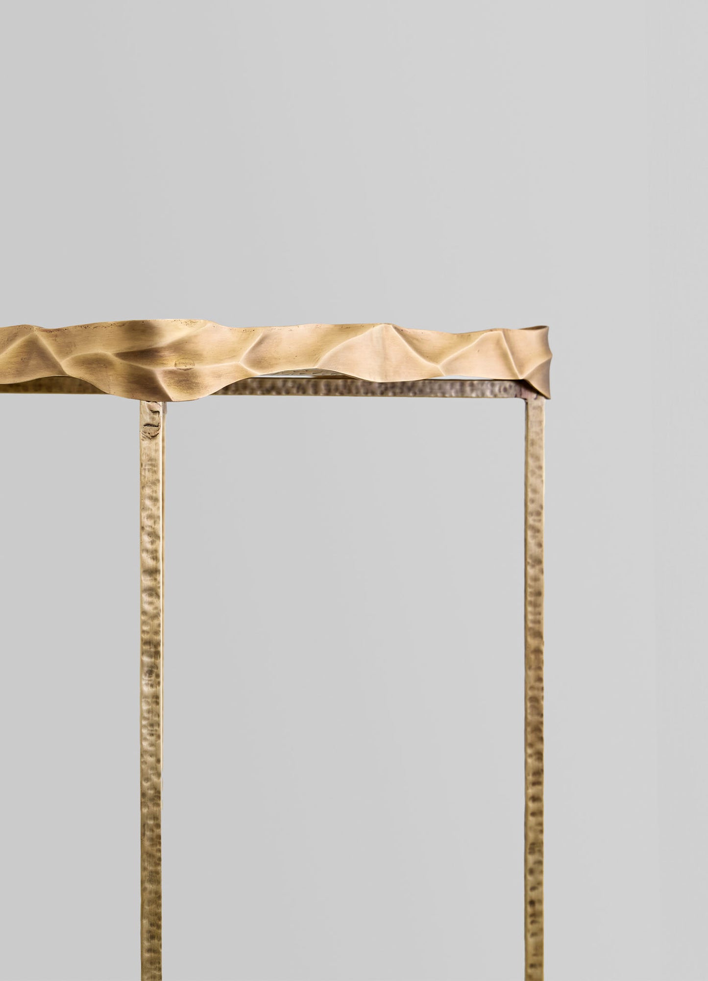 A metal console table with a hammered, textured finish and slender, vertical legs, topped with a crumpled beige fabric or paper sheet.