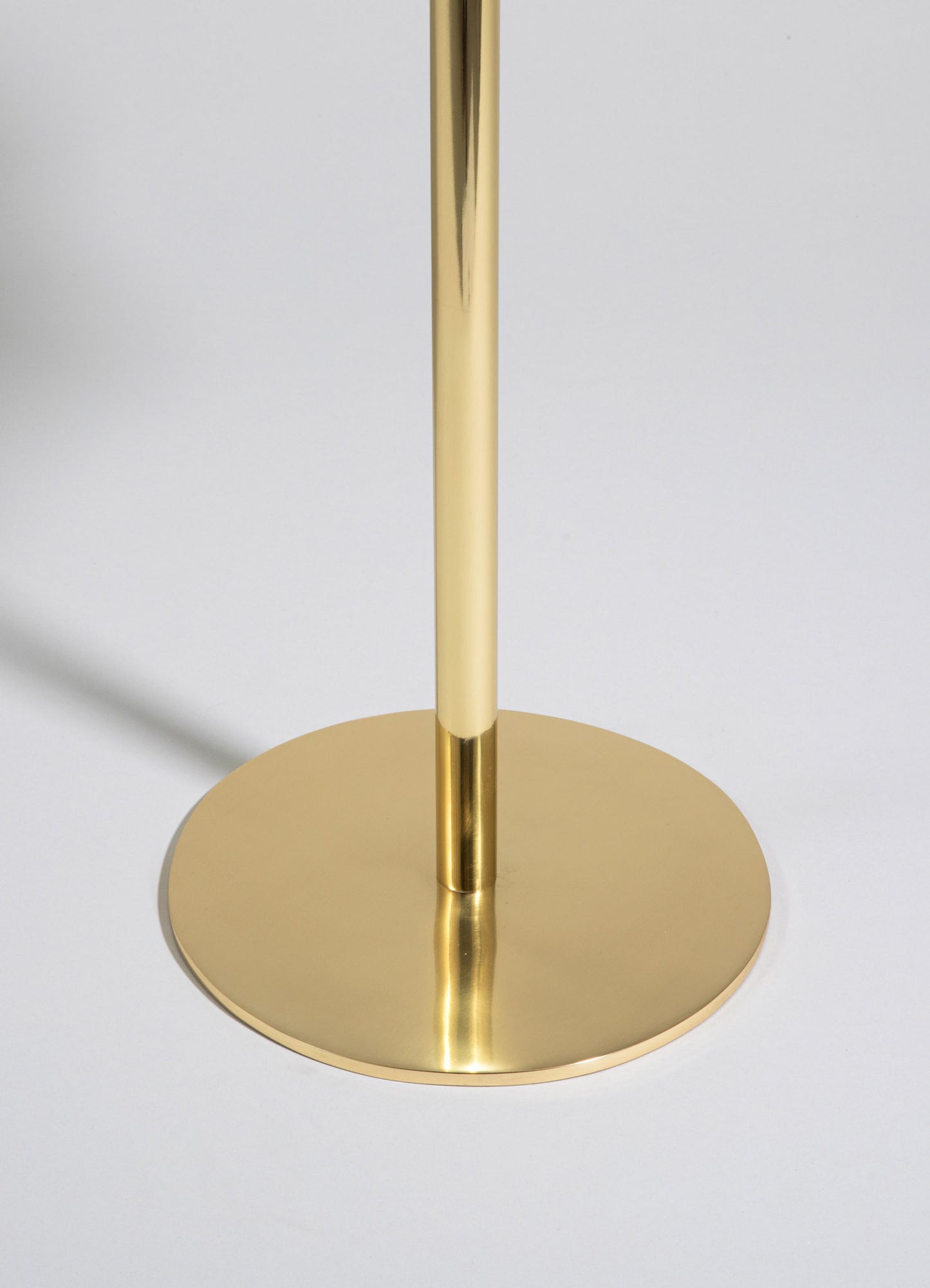 A close-up of a gold-colored metal stand with a circular base and a vertical pole, featuring a smooth and reflective finish. The design is minimalist and contemporary.