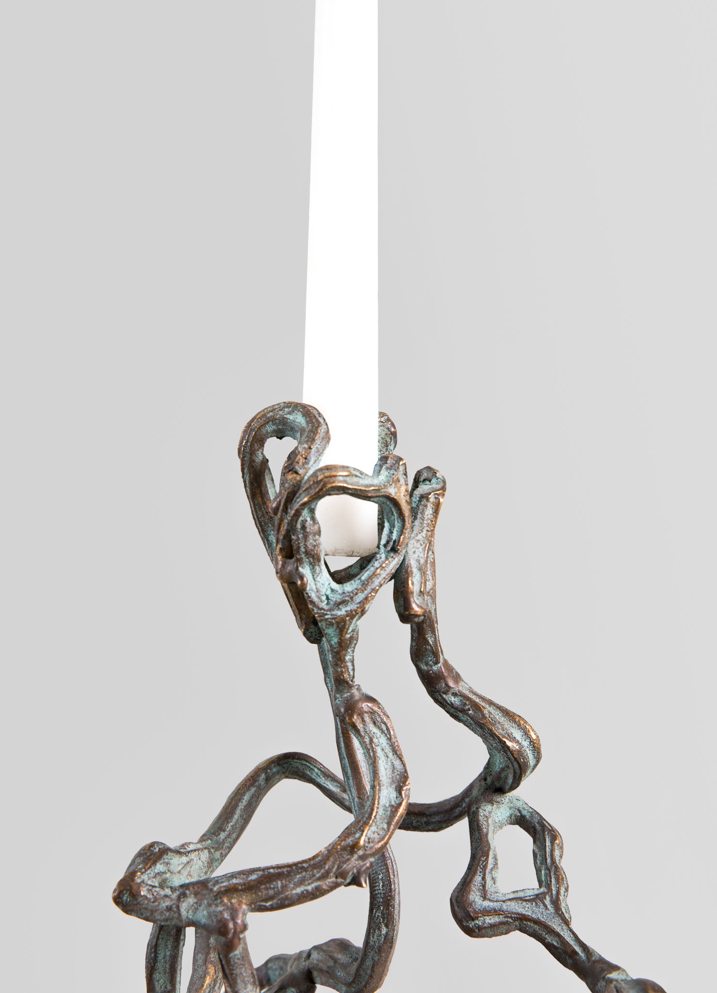 A modern chandelier with a rustic, oxidized metal finish featuring intertwined, branch-like arms. The fixture has a single white candle-shaped bulb and is set against a plain light gray background.