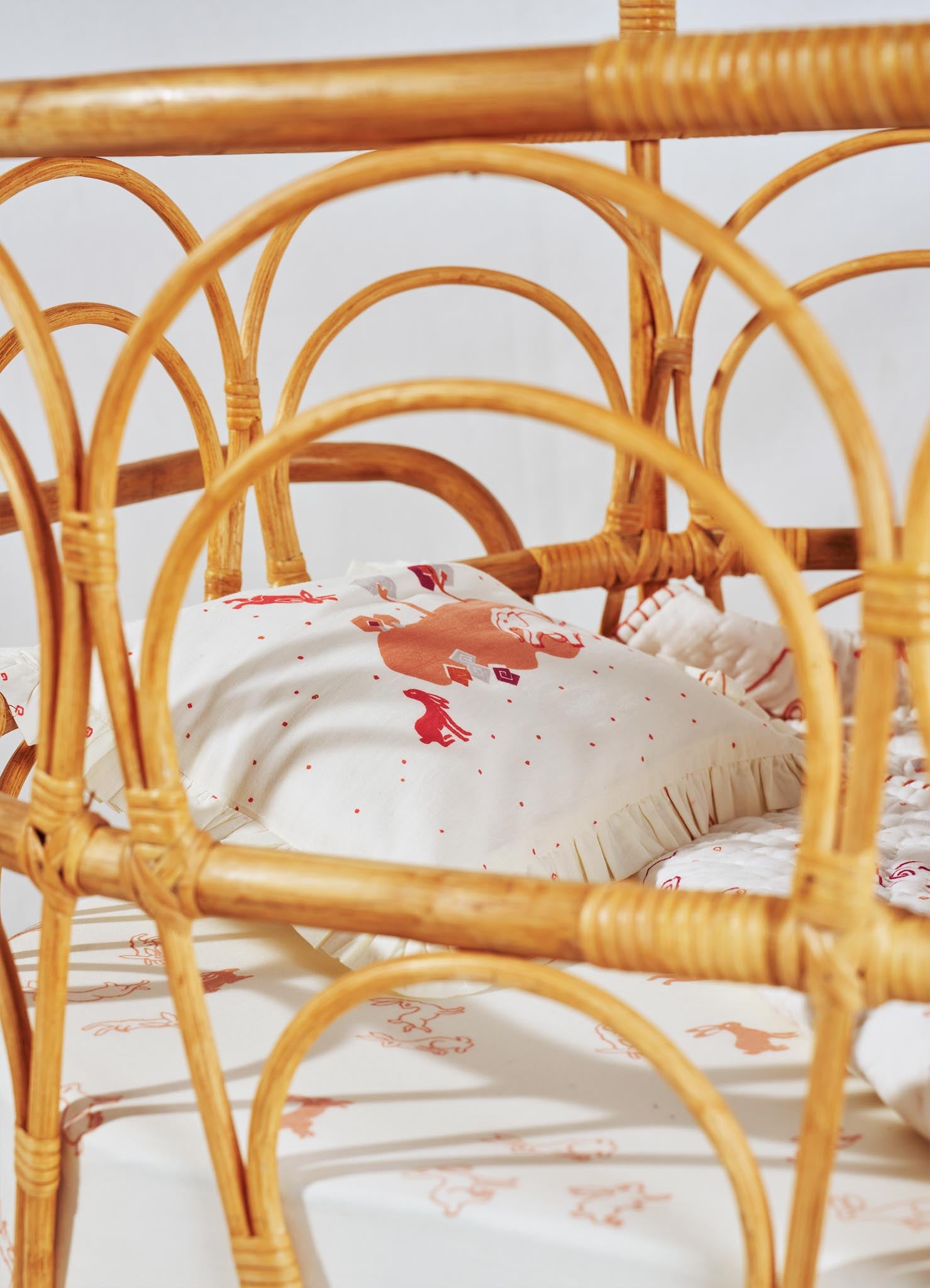 Wicker bed with rounded arch frame and natural rattan material, featuring bedding with a white background and red animal and geometric motif pattern.