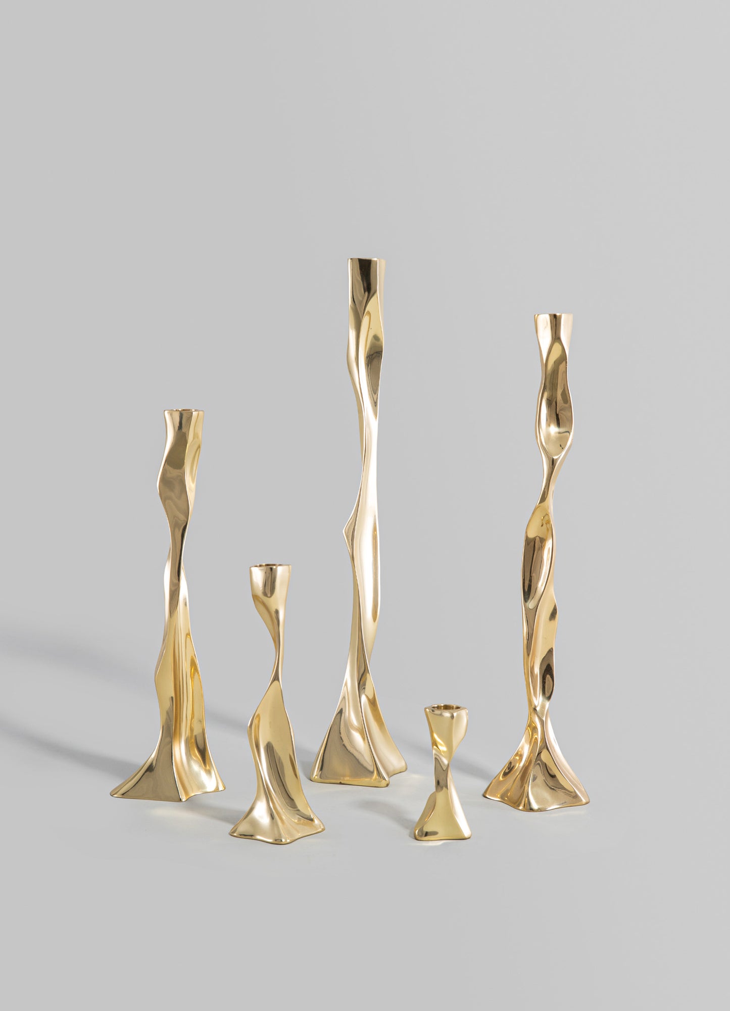 Set of six decorative brass vases with an organic, twisted design and a polished gold finish, varying in height from small to tall. The vases feature a contemporary style with smooth, flowing lines against a plain background.