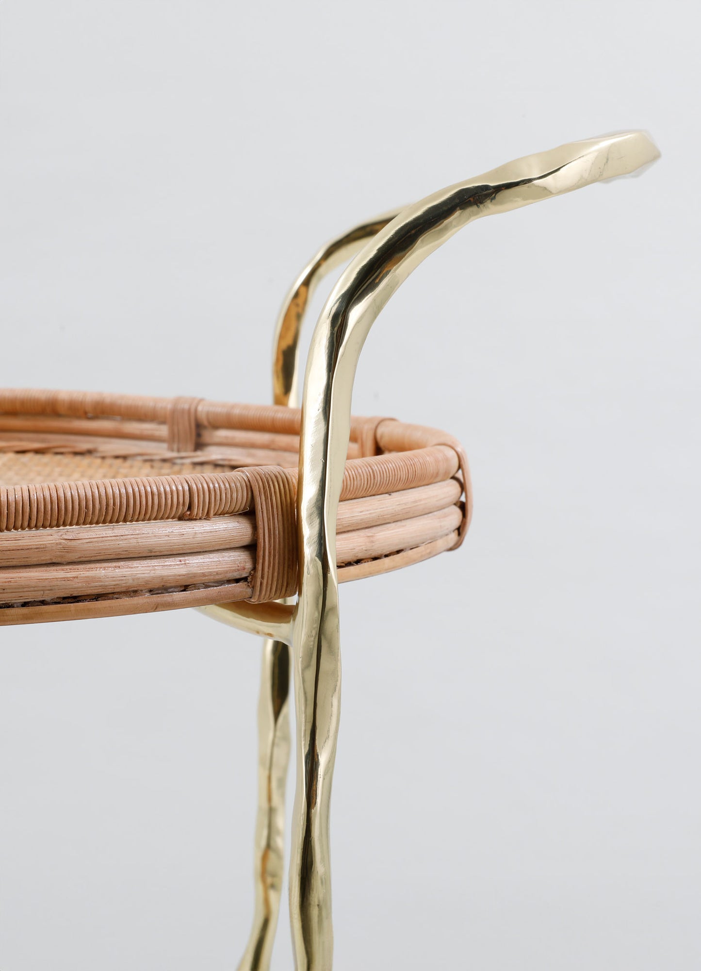 Close-up of the VIYA Assam Brass & Cane Trolley, showcasing woven cane and curved, wavy-textured brass rods in a round design, set against a plain light background.