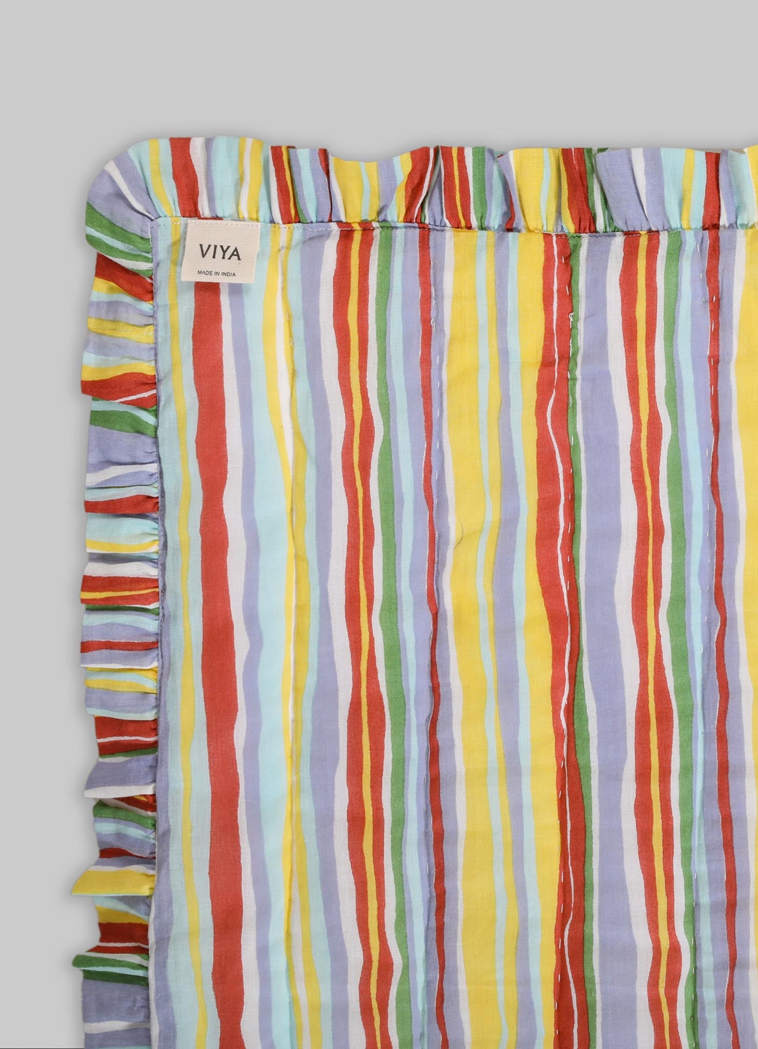 Striped cotton fabric with multicolored vertical lines in red, yellow, green, blue, and lavender, featuring ruffled edges and a small fabric label. The design has a casual, playful mood with bright, vivid tones.