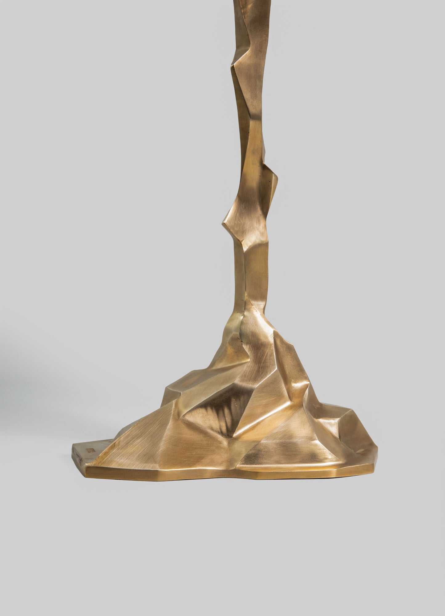 A sculptural table lamp with an abstract, geometric design in a metallic brass finish, featuring angular and faceted surfaces.