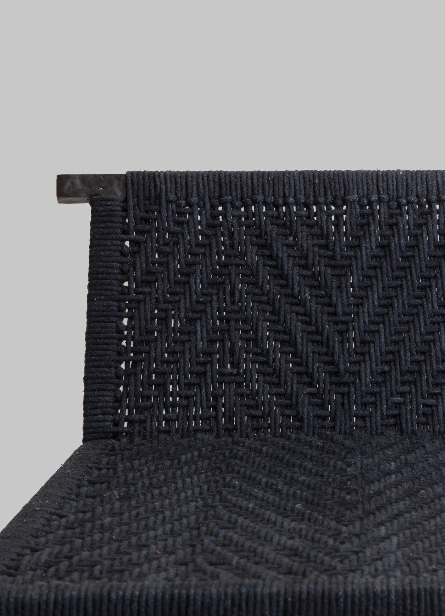A close-up of a woven chair backrest with dark navy or black textile material, featuring a geometric pattern and a matte finish. The upper part appears to have a wooden or similar solid support structure.