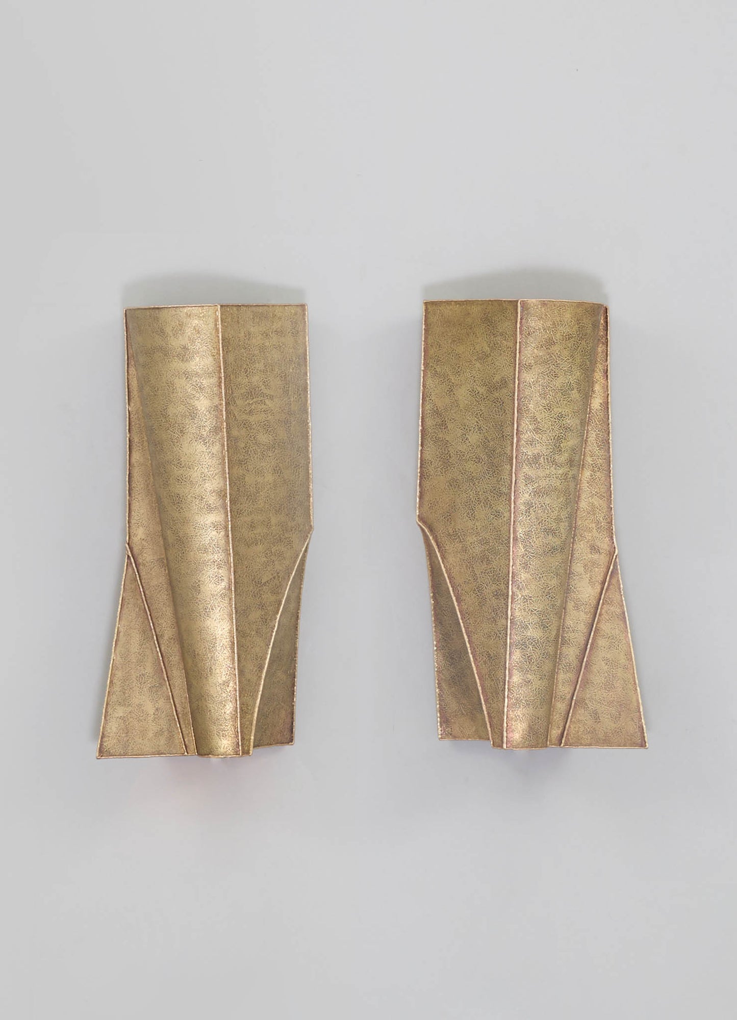 Pair of brass wall sconces with geometric, angular design and a textured matte finish, mounted on a plain light background.