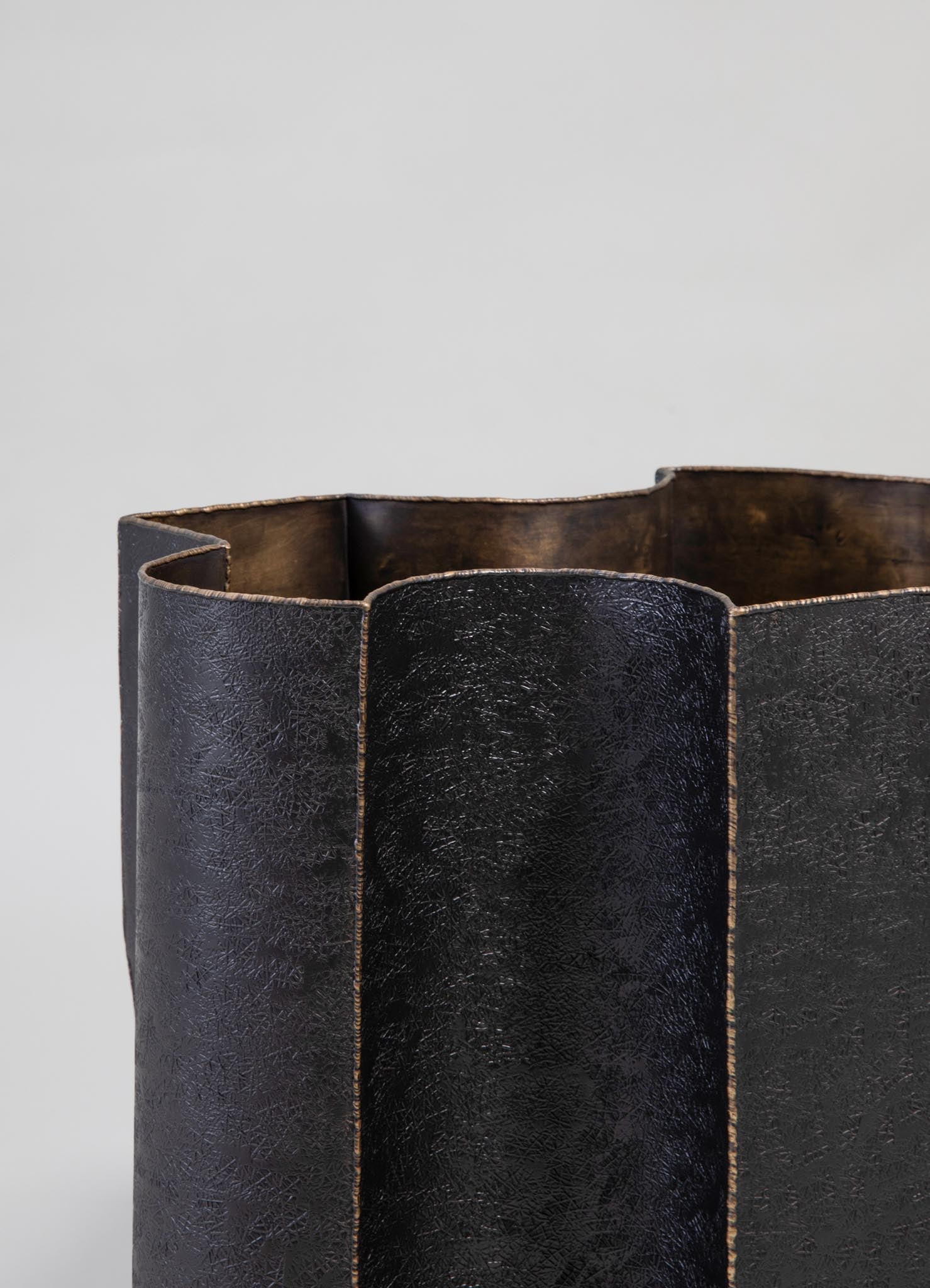 A cylindrical black leather tote bag with a textured surface and visible seam details, featuring a slightly irregular top edge and a warm-toned interior lining.