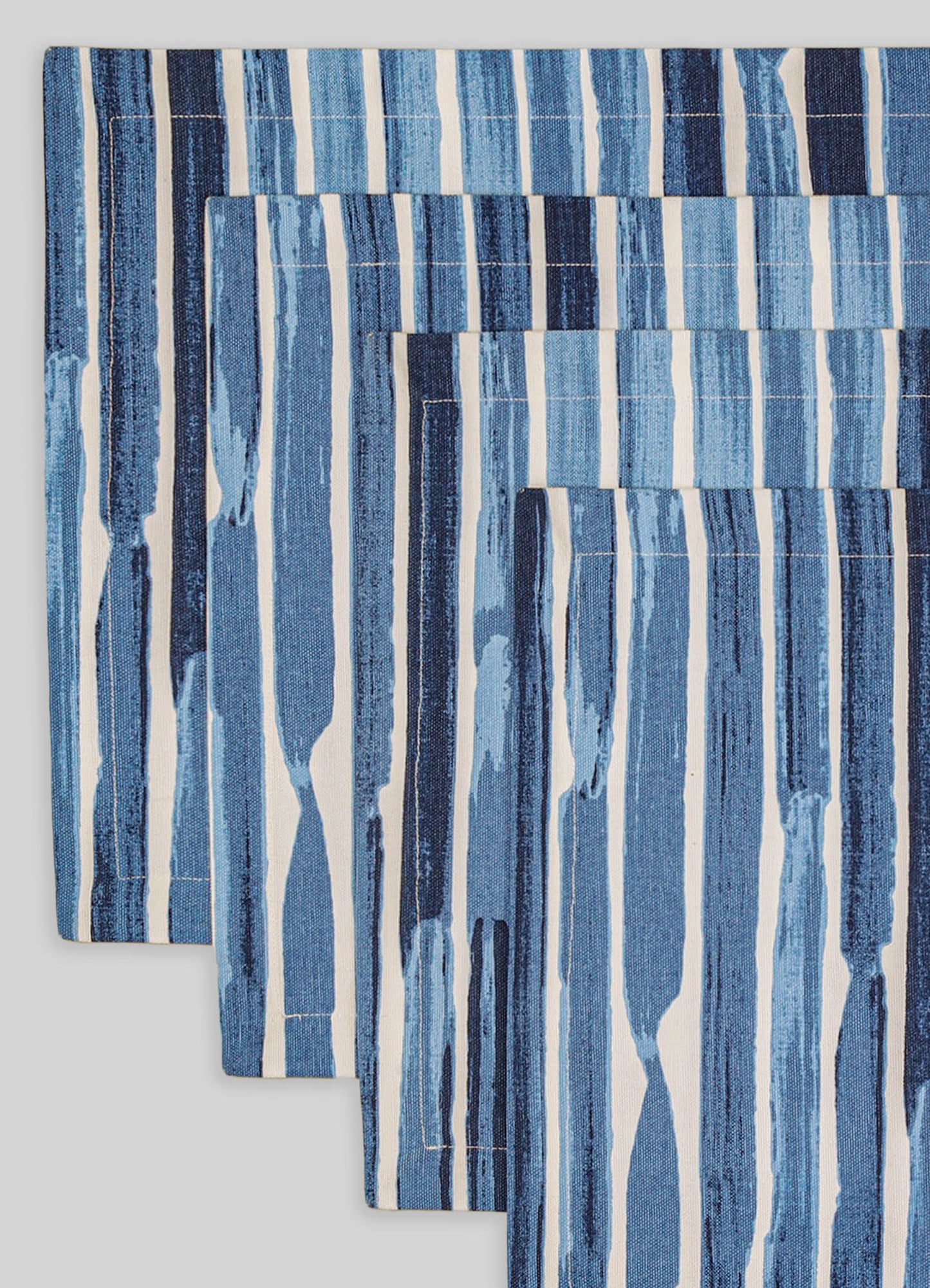 Handwoven textile with vertical blue and white stripes, featuring a patchwork design and varying shades of blue in a casual, contemporary style.
