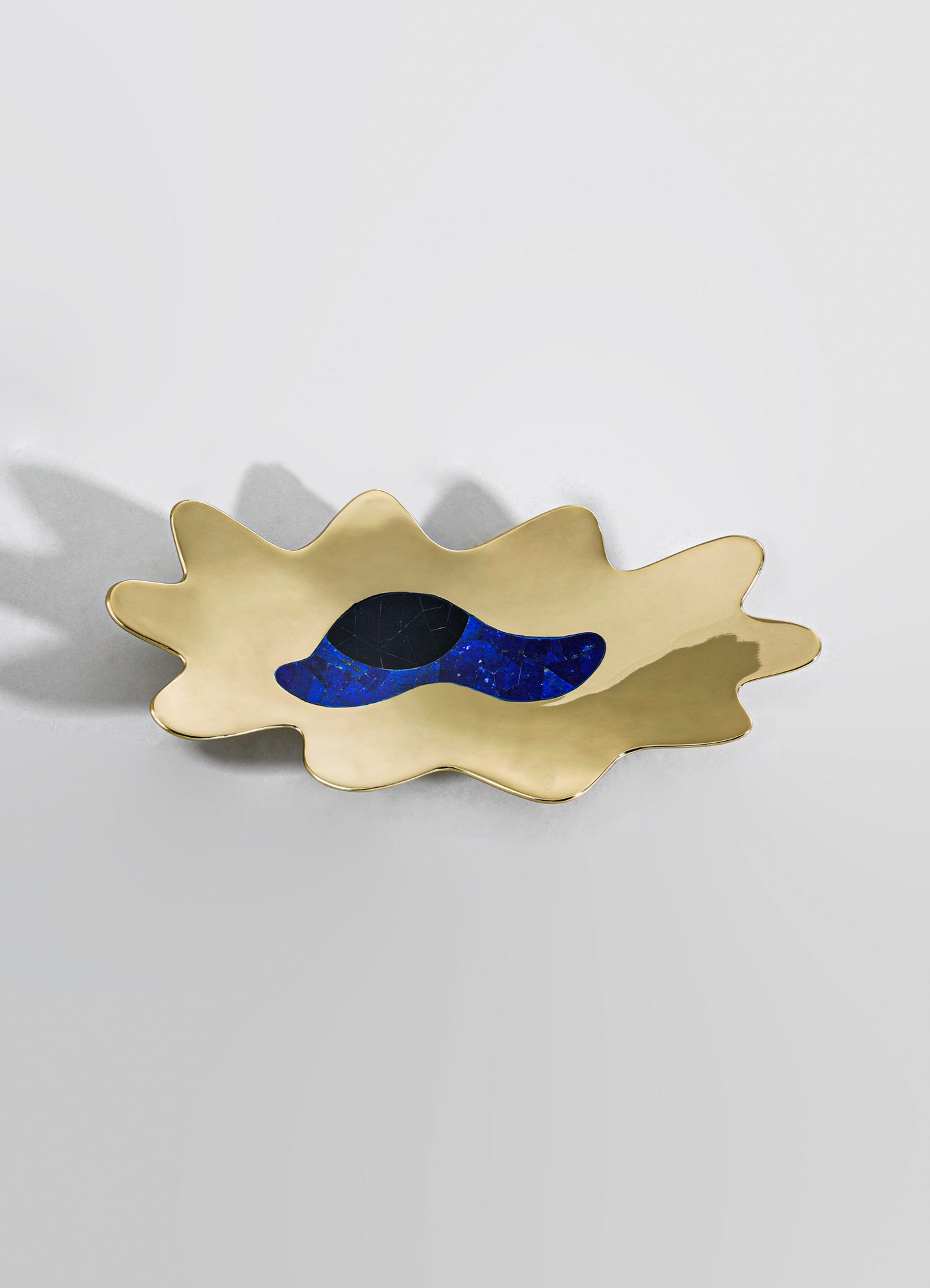 A decorative ceramic dish with an organic, leaf-like shape and a glossy gold finish, featuring a central motif in deep blue and black tones. The design evokes a modern artistic style with smooth, flowing contours.