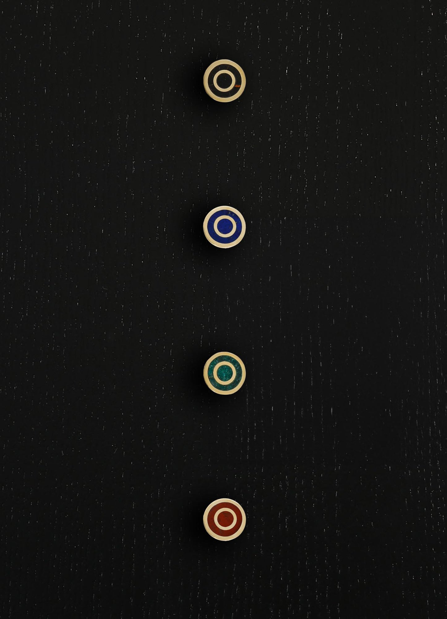 Glass knobs with concentric circle motifs in metallic gold, blue, green, and red, mounted on a dark textured surface. The design features a contemporary aesthetic with bold colors and geometric patterns.
