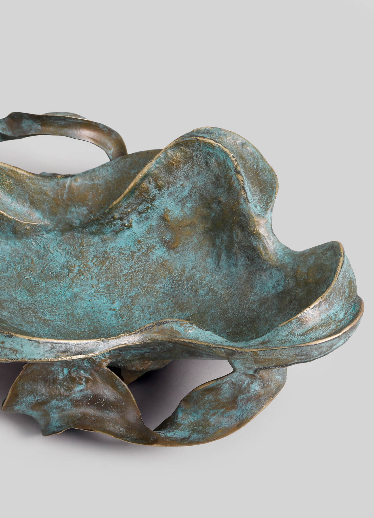 A metal bowl with a textured, oxidized finish in shades of teal and bronze, featuring an organic, irregular shape with wavy edges and a raised, curled rim.