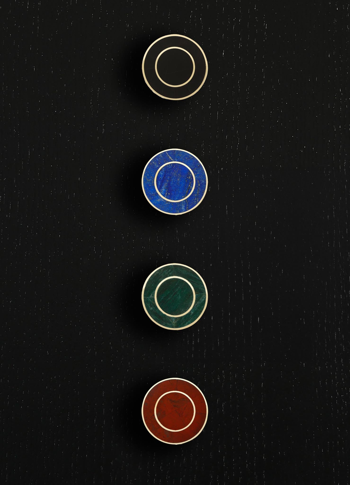 Four circular decorative objects with metal rims and colorful, textured centers in black, blue, green, and red hues, mounted on a black wall with a dotted texture.