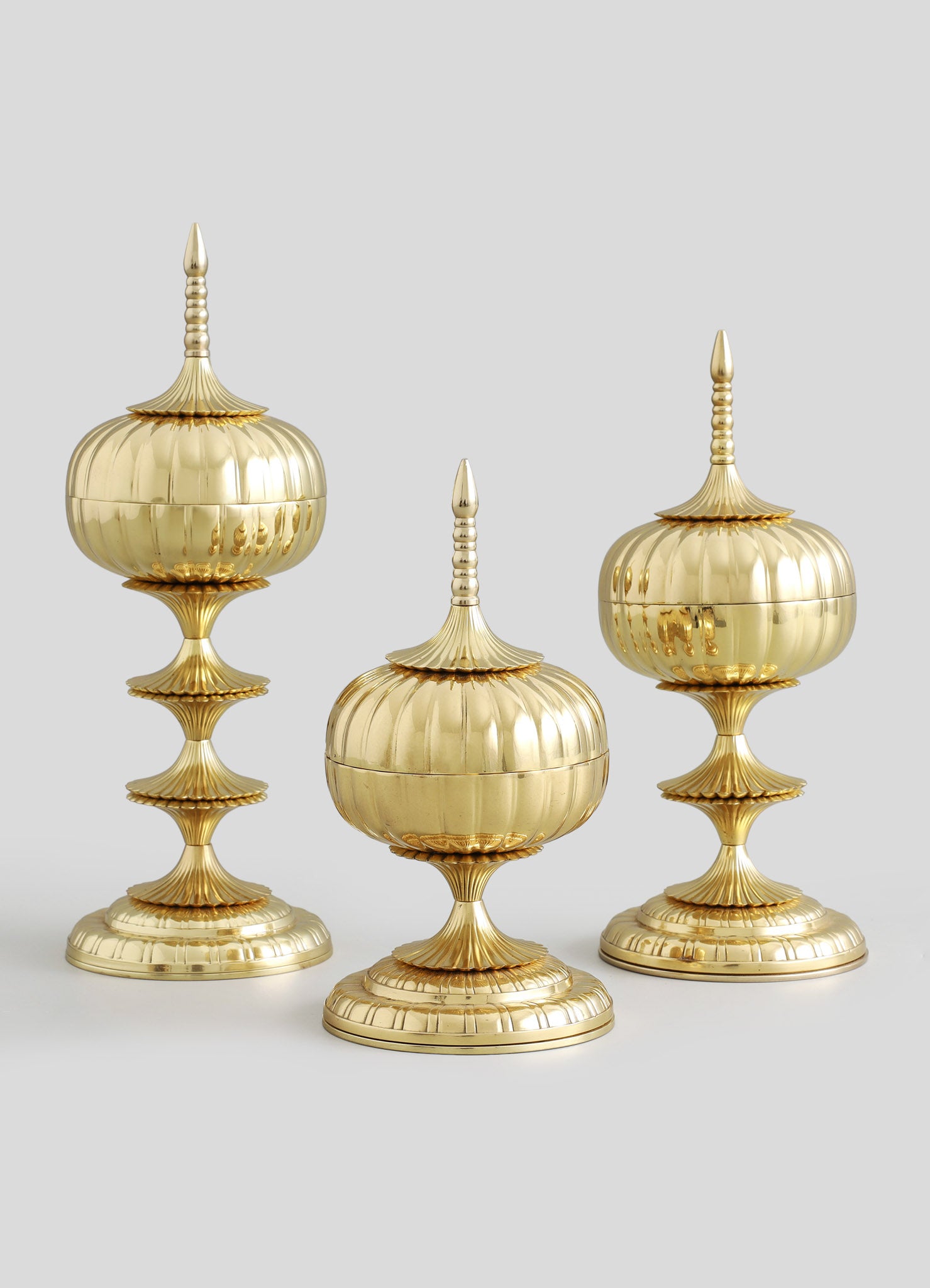 Three decorative finials made of polished gold-colored metal with ribbed and fluted designs, featuring pointed finial tops and rounded, layered bases. The finials have a vintage or classical style with an ornate, luxurious appearance.