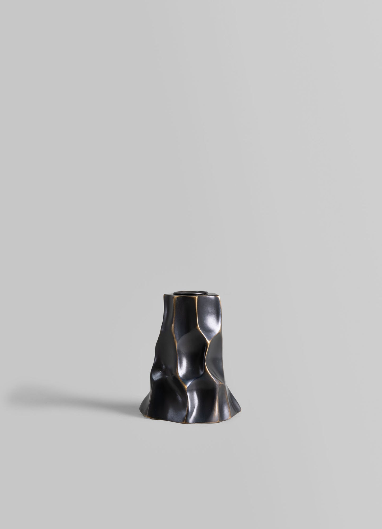 A black ceramic vase with an irregular, textured surface and metallic gold accents, featuring an organic, sculptural form against a plain gray background.