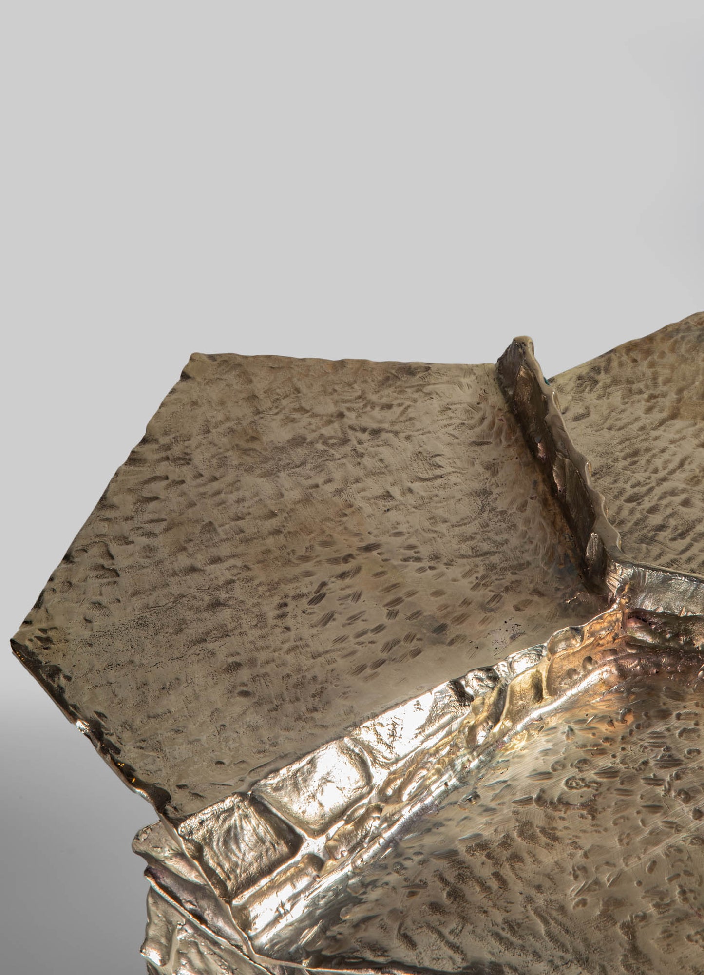 Metallic silver tray with hammered texture and irregular edges, featuring a raised brick-like border along one side, on a plain background.