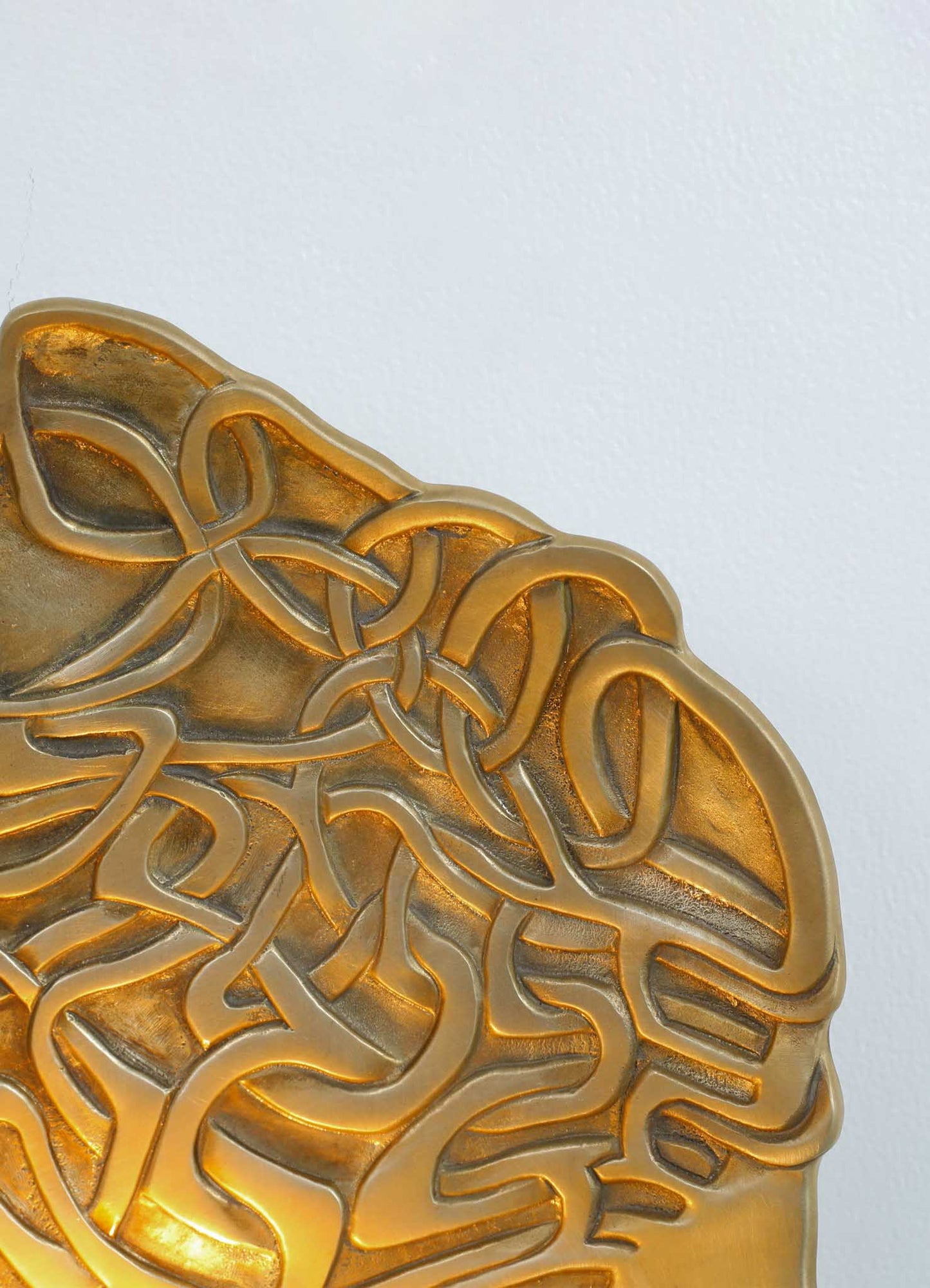 Decorative brass tray with an intricate, swirling knot motif and a polished gold finish, suitable for display or serving in a luxury interior setting.