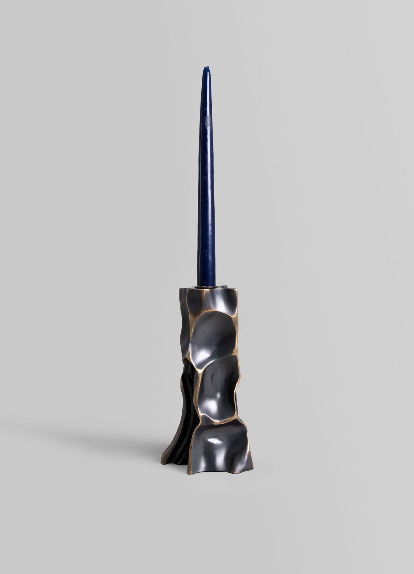 A candle holder with an irregular, sculptural design in metallic silver and black tones, holding a tall, dark blue taper candle.