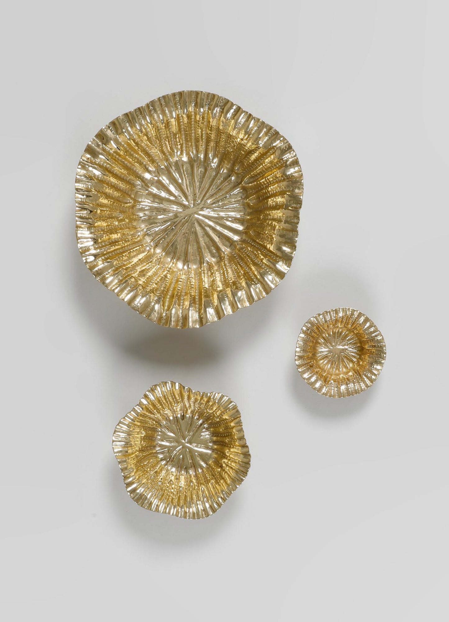 Set of three metallic gold bowls with a textured, ribbed surface and scalloped edges, made of glass or metal, featuring a reflective finish. The bowls vary in size and are arranged on a plain light background, emphasizing their contemporary and decorative style.