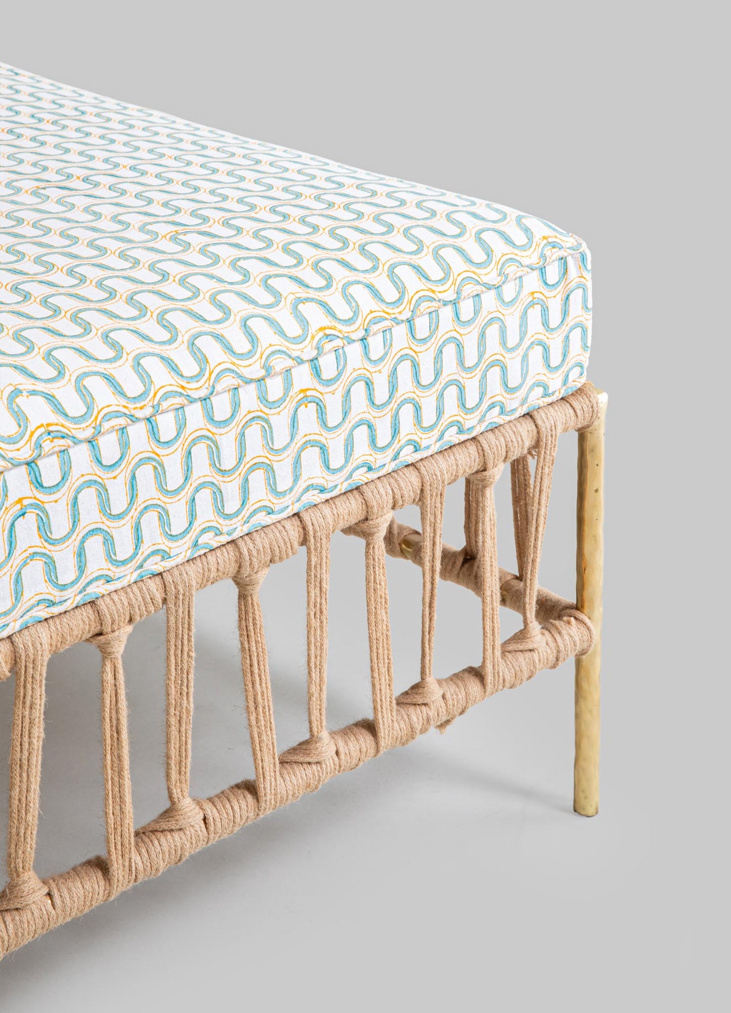 Woven rattan bench with a patterned fabric cushion featuring a geometric blue and yellow motif, supported by a natural bamboo frame.